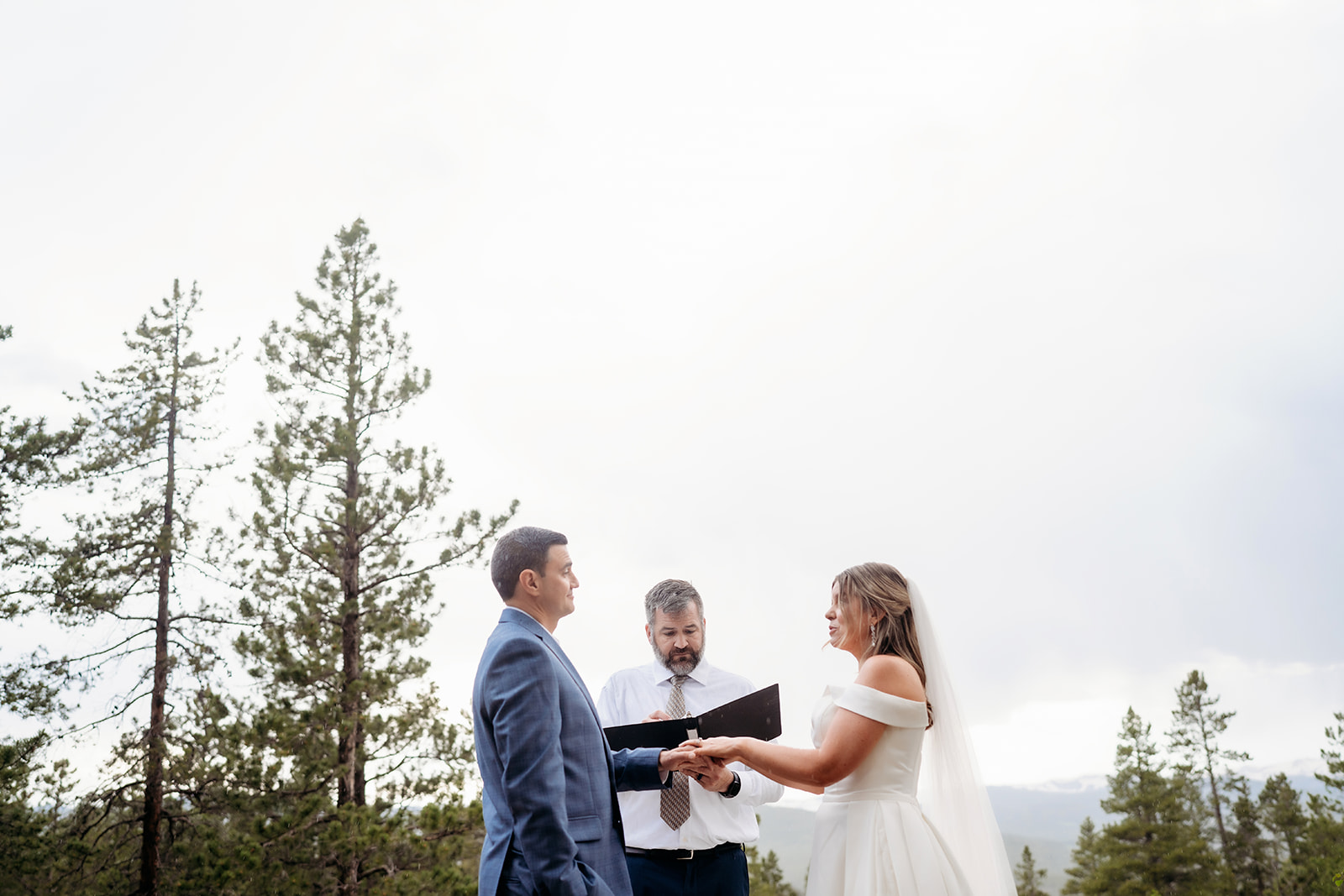 Bride and groom holding hands with officiant under tall pine trees during their Colorado adventure elopement ceremony.