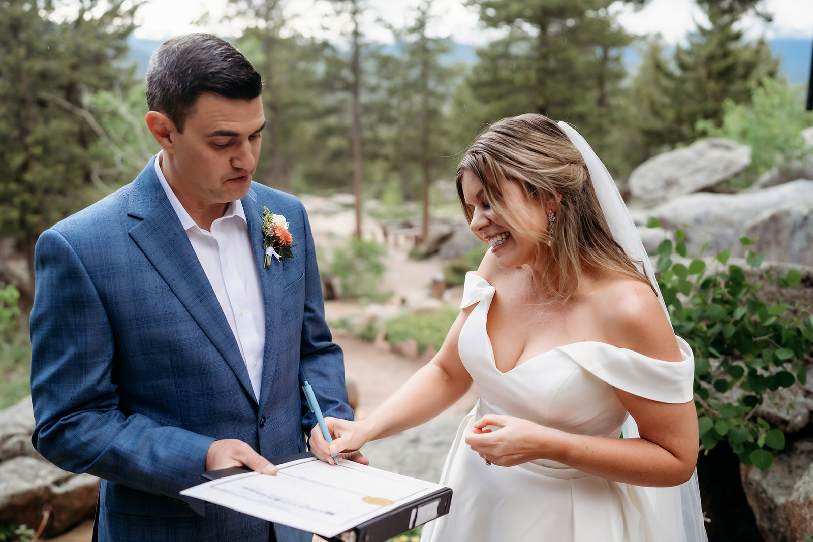 Bride signing marriage license with groom holding papers during their Colorado adventure elopement.