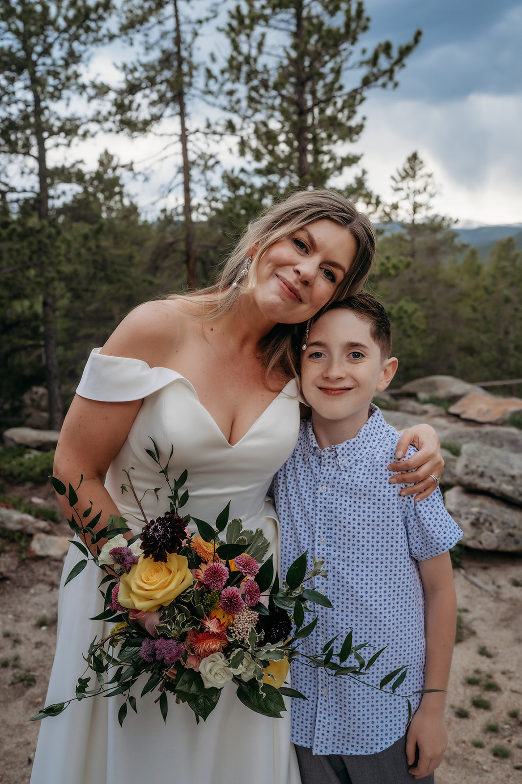 Bride hugging her son and smiling with bouquet in hand at their Colorado adventure elopement.
