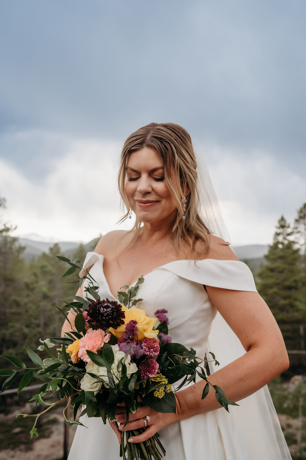 Bride holding colorful bouquet of wildflowers and smiling softly at her Colorado adventure elopement.