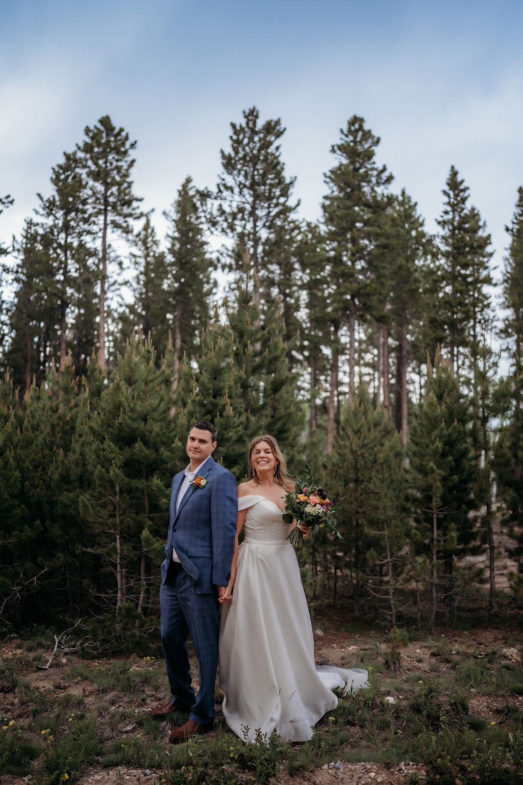 Bride and groom holding hands with pine trees behind them during their Colorado adventure elopement.