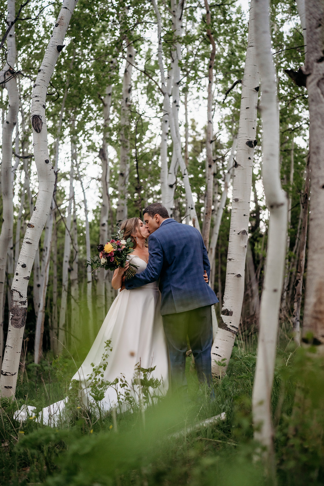 Bride and groom sharing a kiss surrounded by tall aspens at their Colorado adventure elopement.
