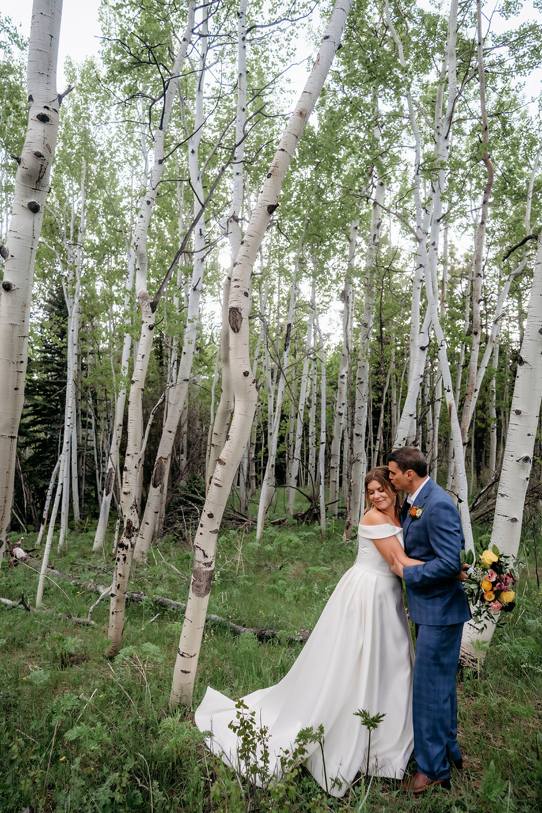 Groom kissing bride’s forehead in an aspen grove during their Colorado adventure elopement.