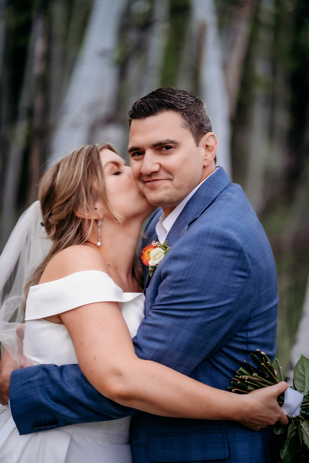 Bride kissing groom's cheek while he embraces her