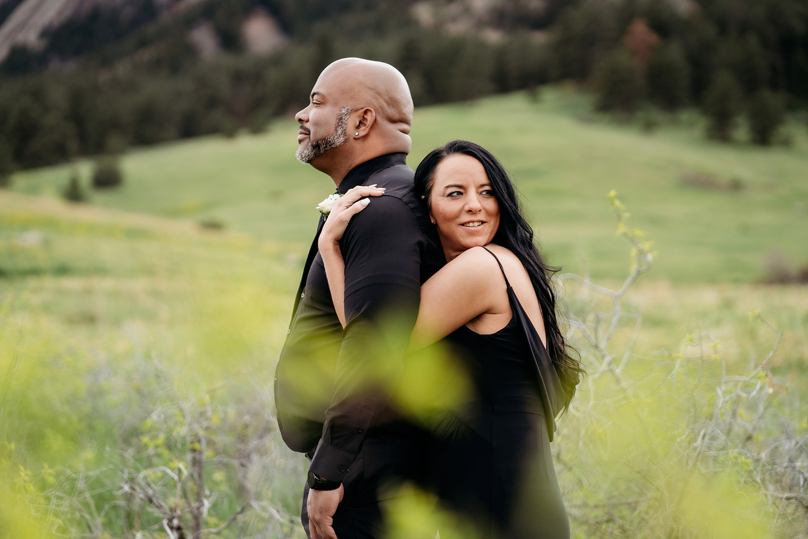 Couple standing back to back in a lush green meadow, the woman looking confidently at the camera during summer engagement photos.