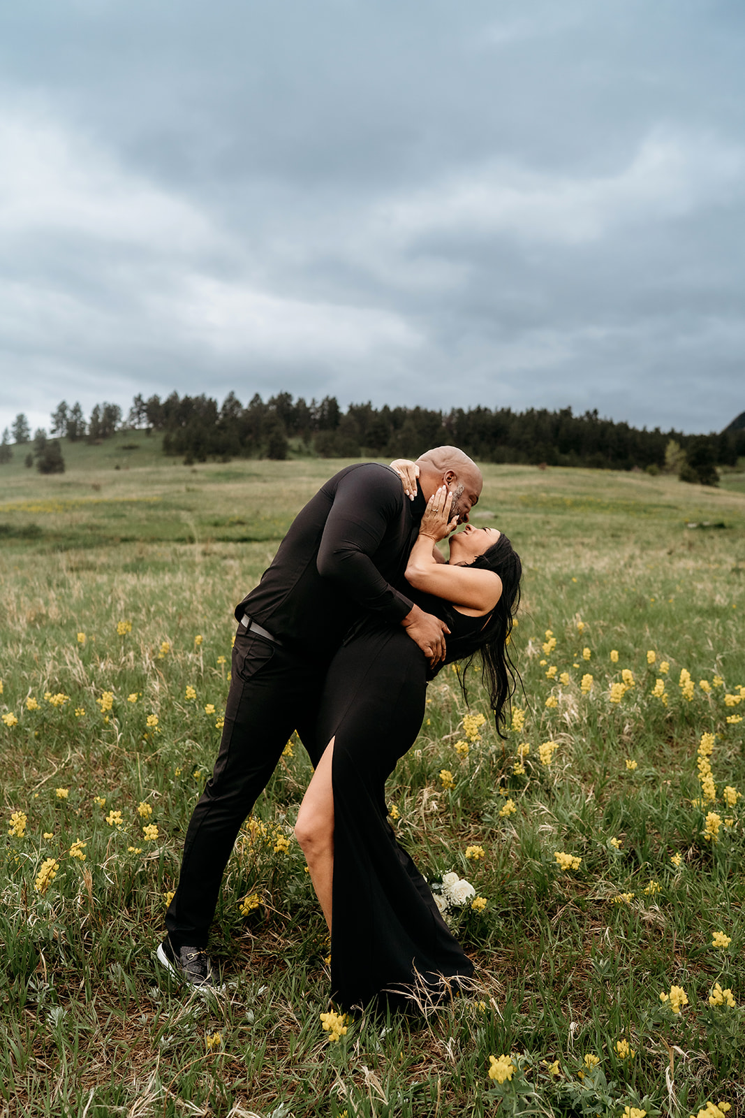 Couple sharing a playful dip kiss in a wildflower meadow during their summer engagement photos.