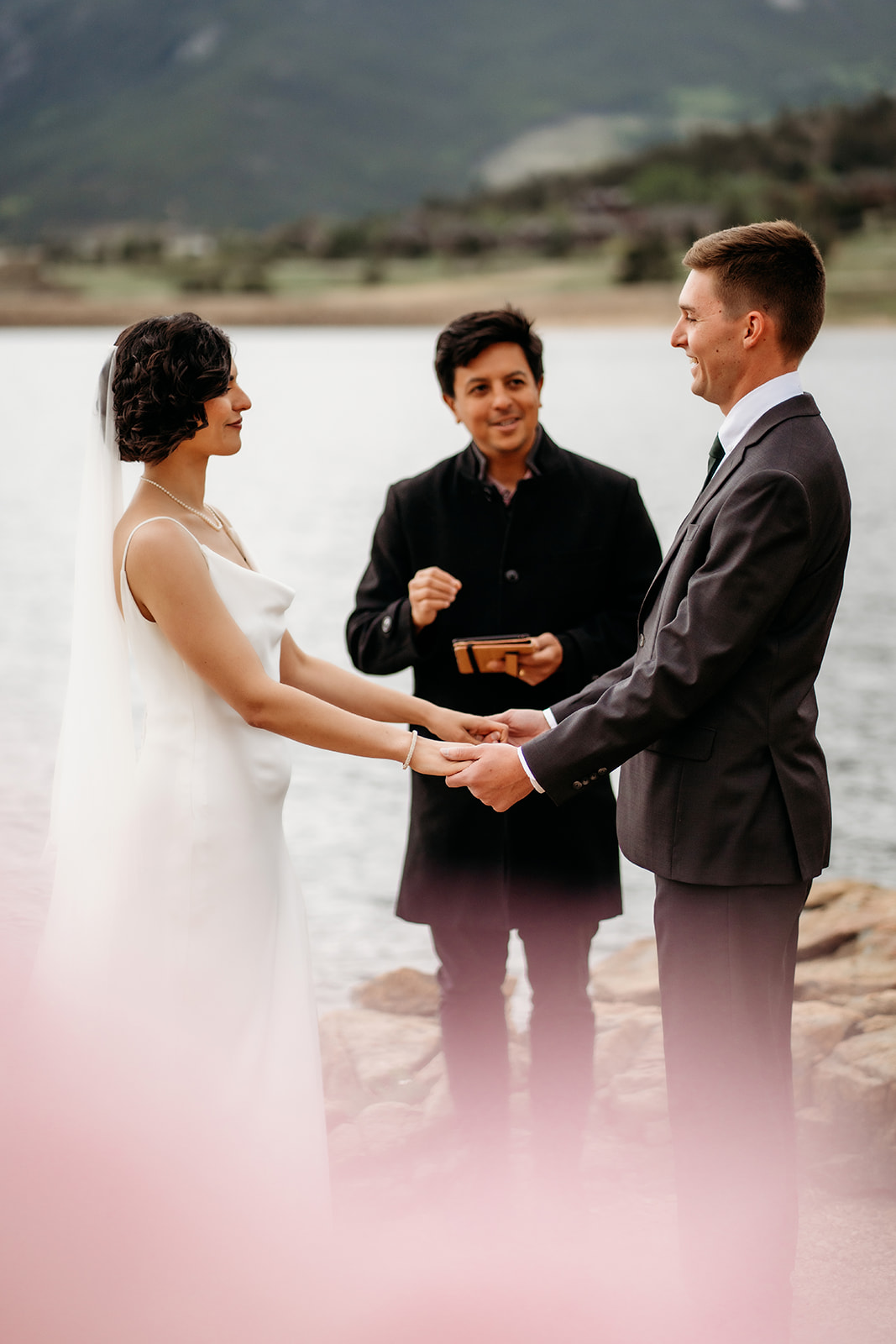 Couple exchanges vows with an officiant overlooking the lake and mountains at a peaceful Colorado elopement location.