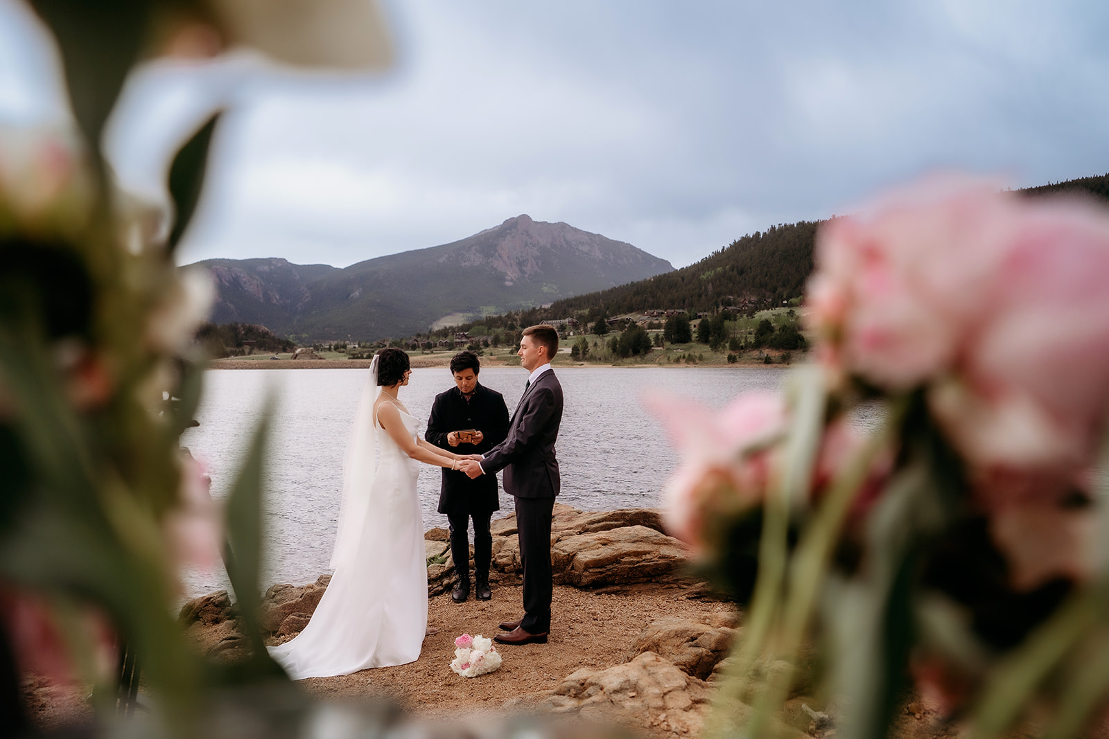 Bride and groom hold hands and lock eyes at the water’s edge, fully present in their intimate elopement moment.
