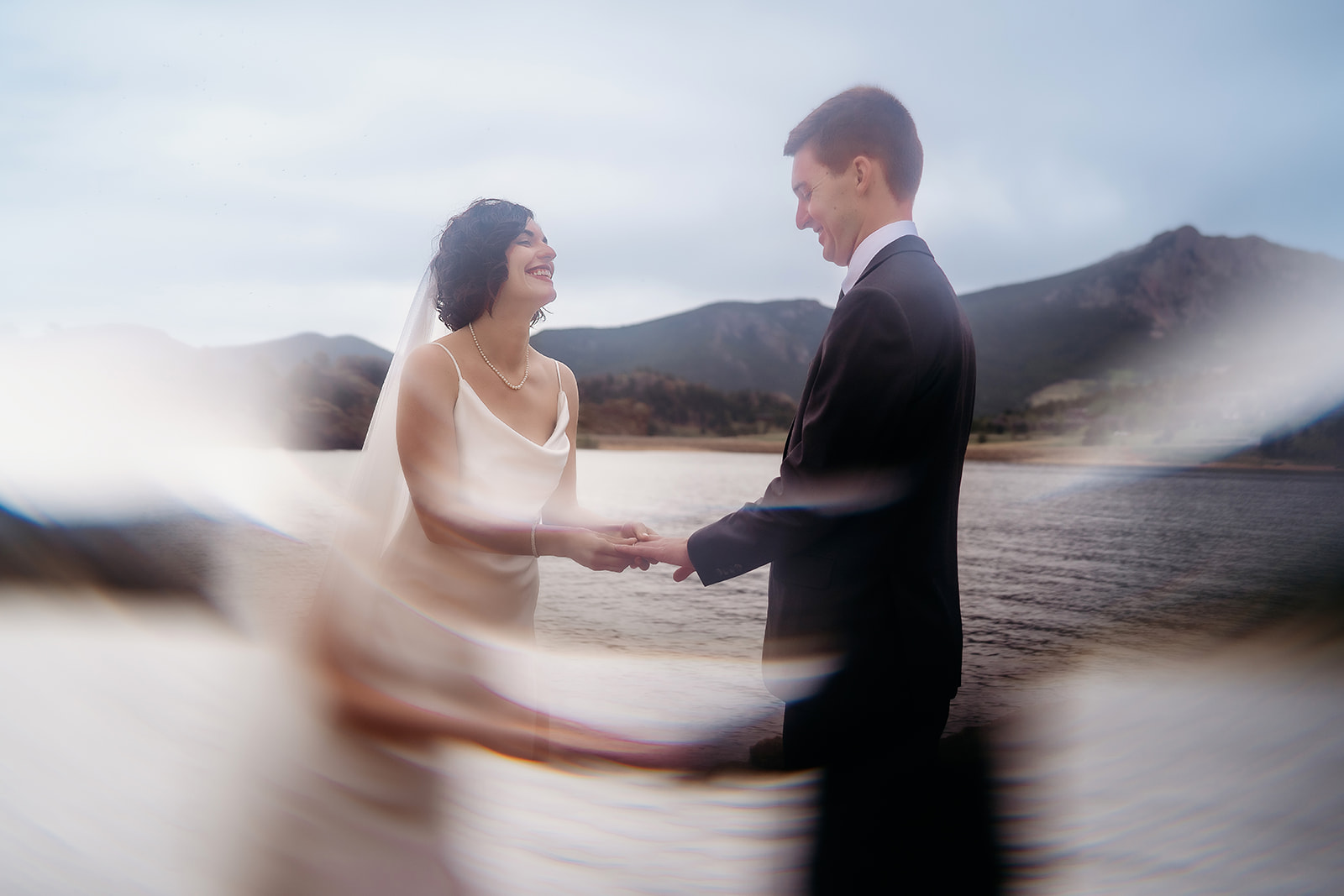 Dreamy photo of the couple holding hands with blurred foreground reflections, celebrating their ceremony at a Colorado elopement location.