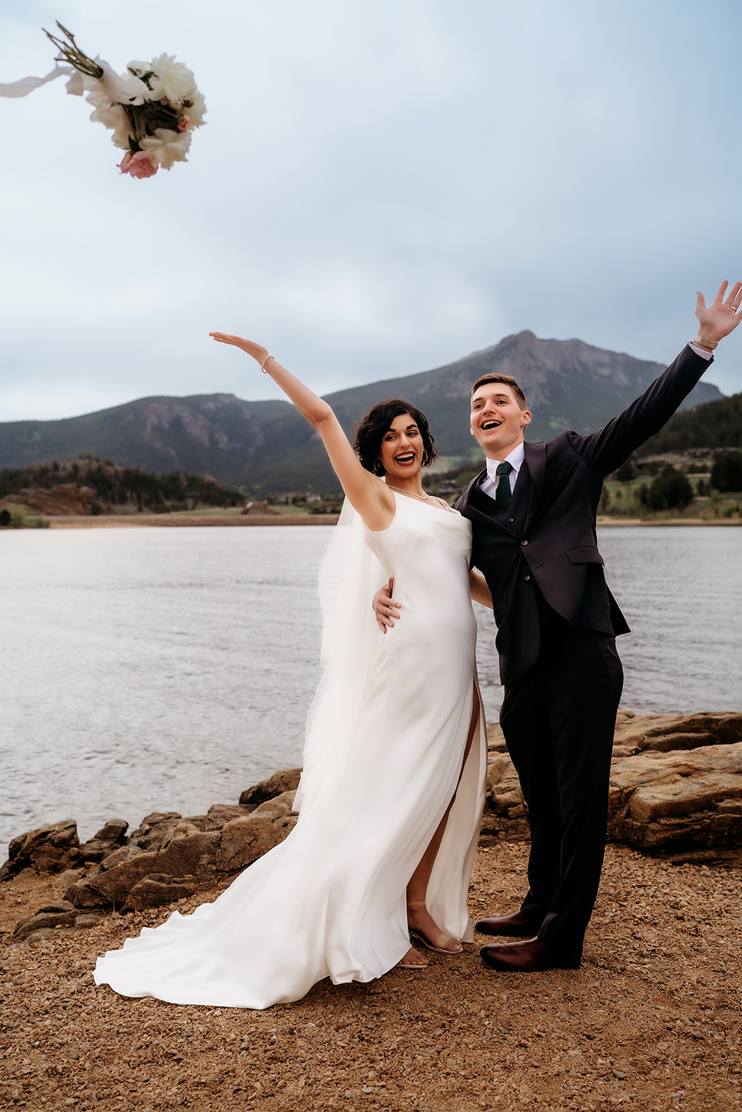 Newlyweds throw the bouquet into the air with excitement after tying the knot beside the lake and mountains.