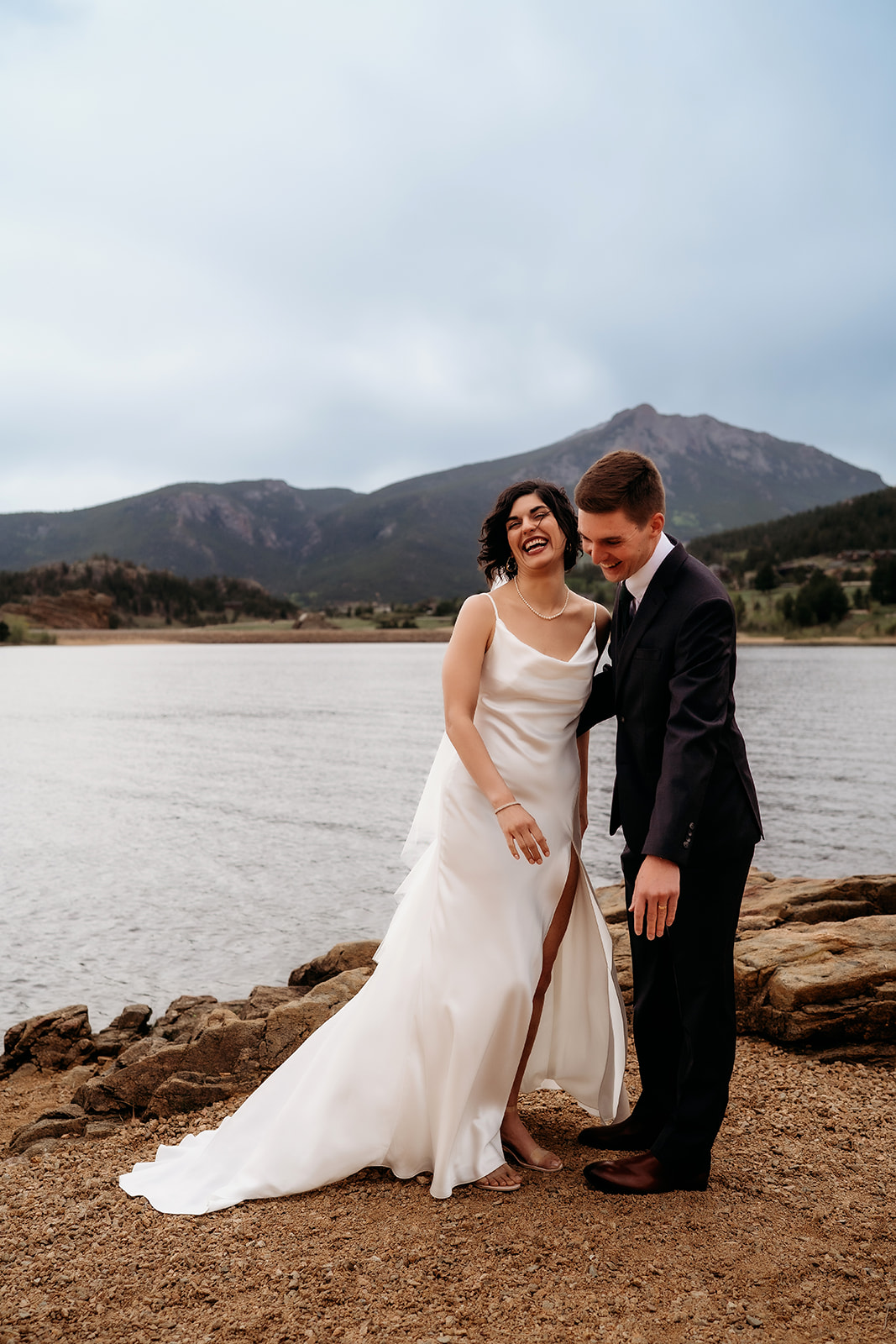 Couple shares a laugh together in front of the lake and mountains, enjoying a candid moment at their Colorado elopement location.