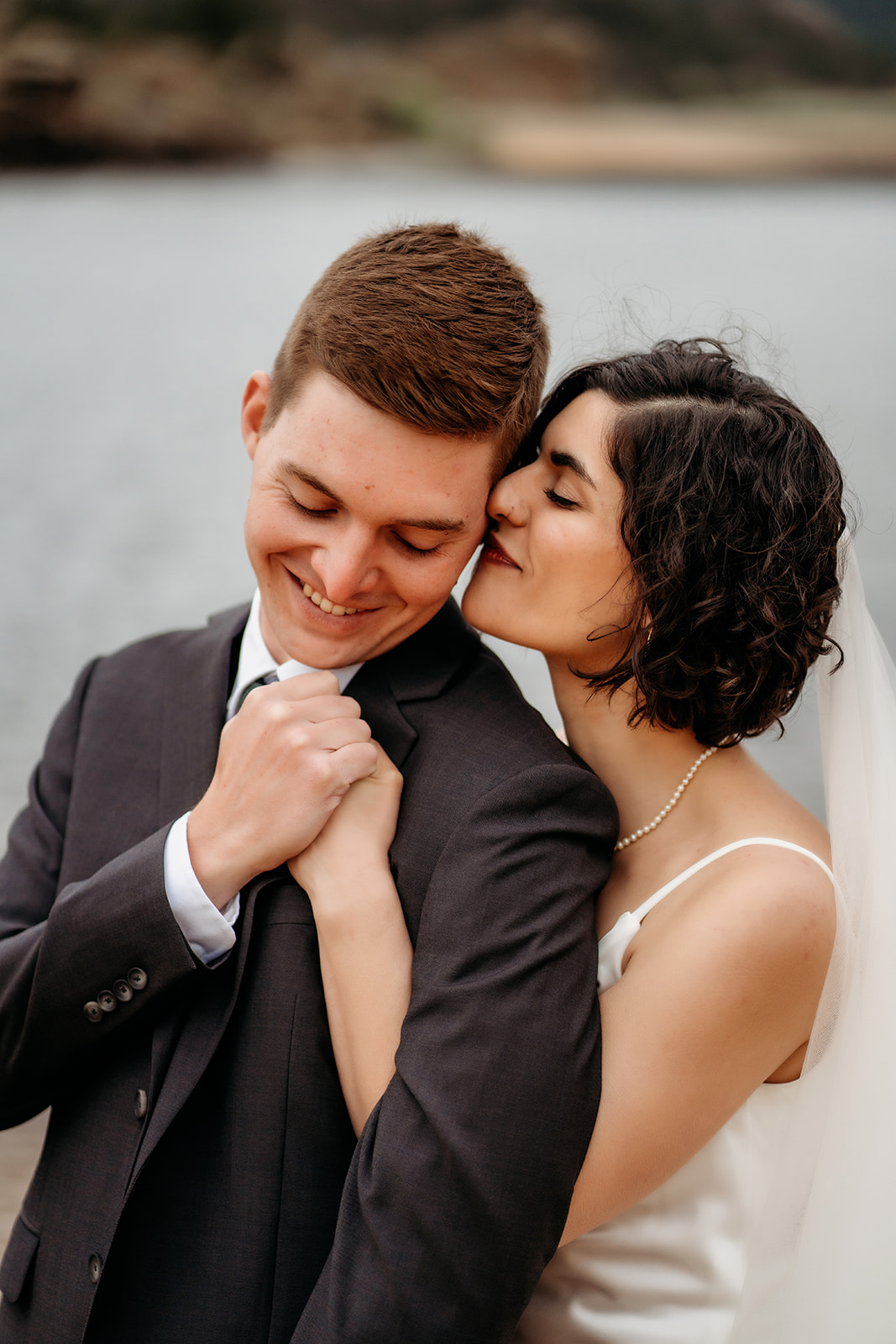 Bride kisses her groom’s cheek while holding his hand close, a candid and tender moment during their intimate wedding day.