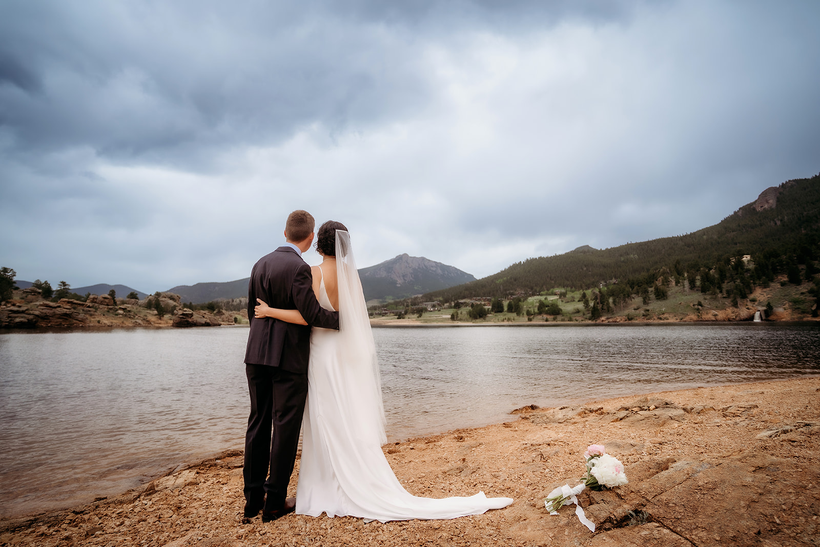 Couple embraces while gazing at the lake and mountains, soaking in their private moment at a peaceful Colorado elopement location.