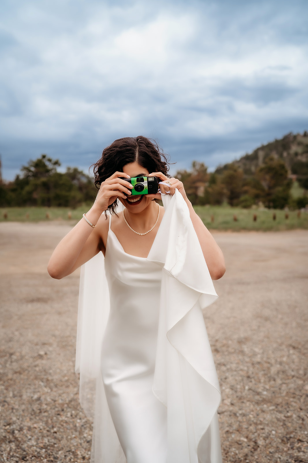 Bride playfully snaps a photo with a disposable camera, adding a fun and personal touch to her lakeside Colorado elopement.