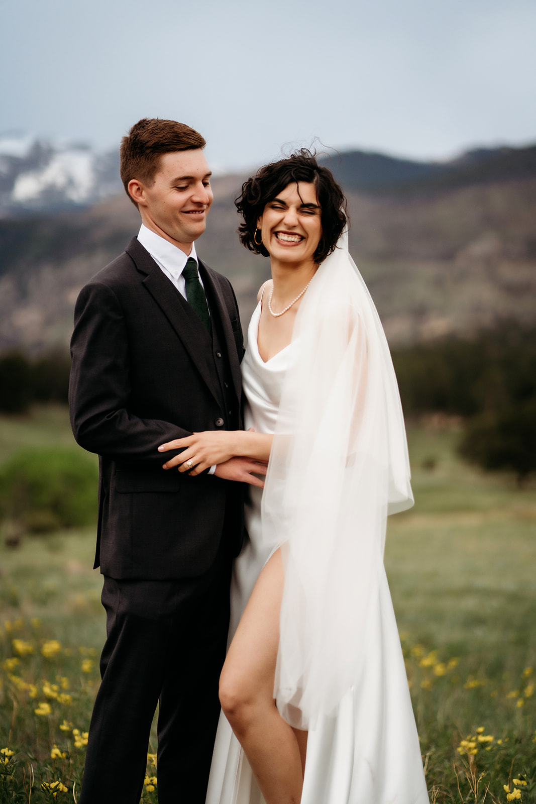 Couple shares a genuine laugh while standing among wildflowers, capturing the joy of their elopement in the Rockies.