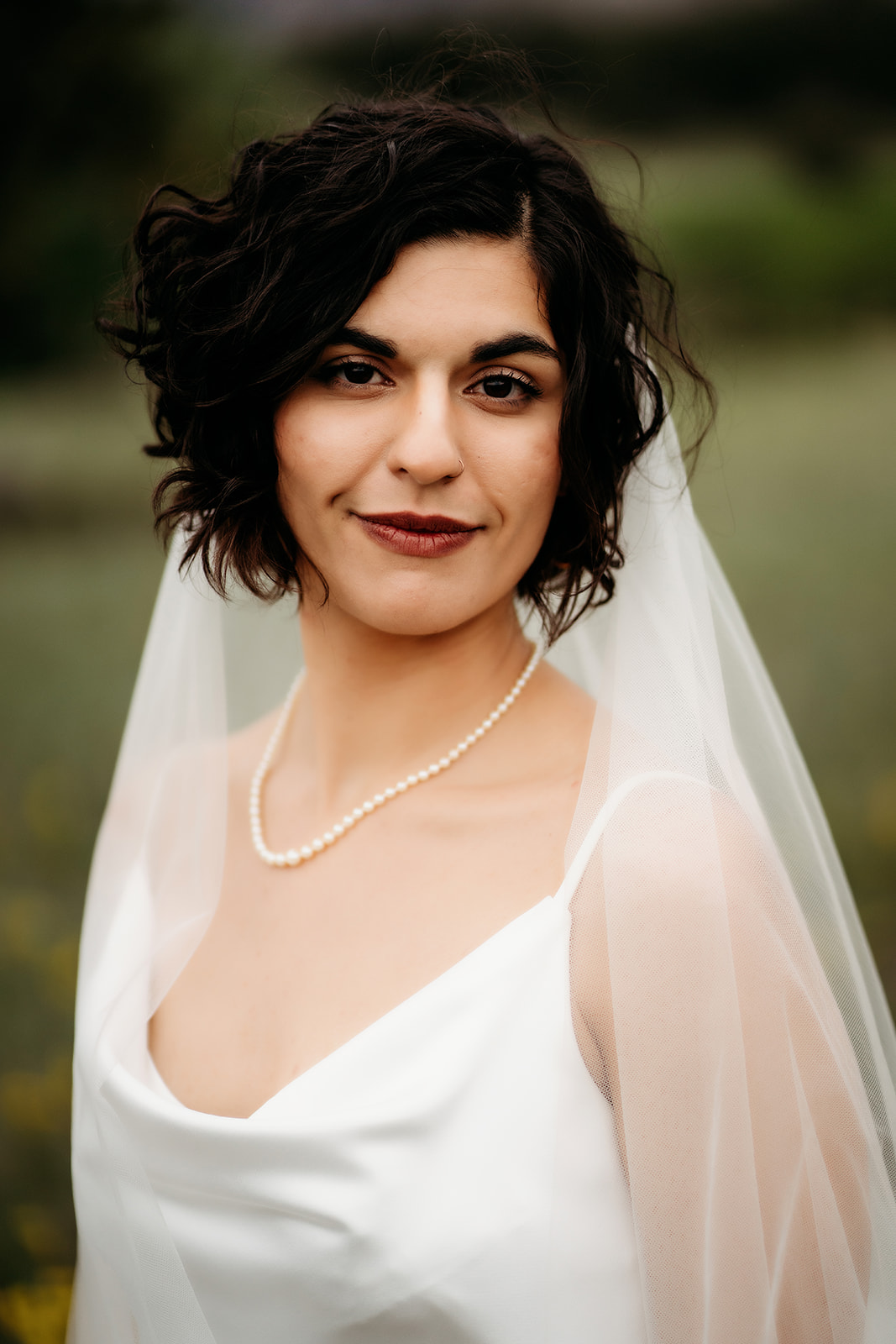 Bride smiles softly at the camera in her flowing gown and veil, her look framed by a natural Colorado backdrop.