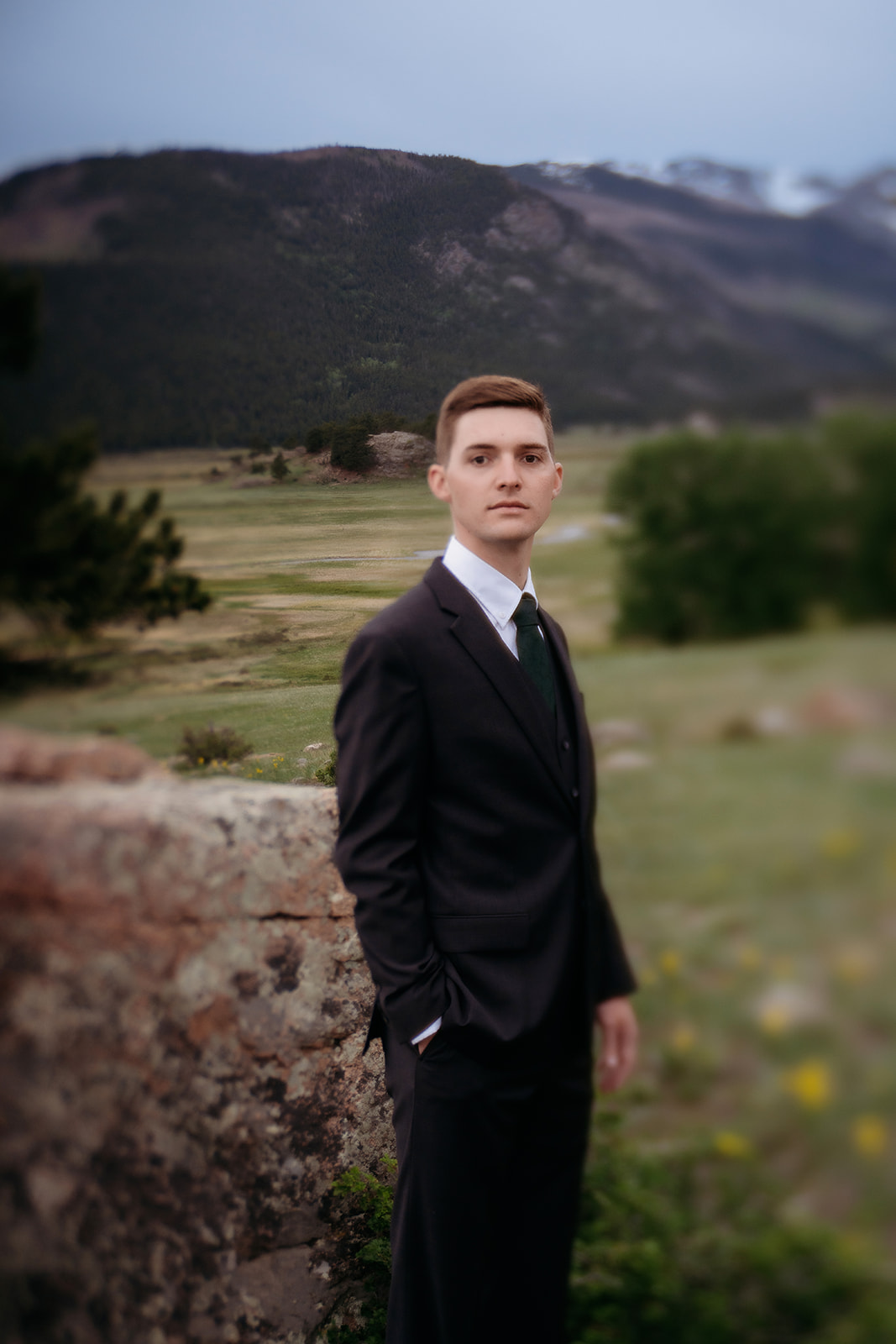 Groom stands confidently in a mountain meadow, with distant peaks hinting at the beauty of Colorado elopement locations.