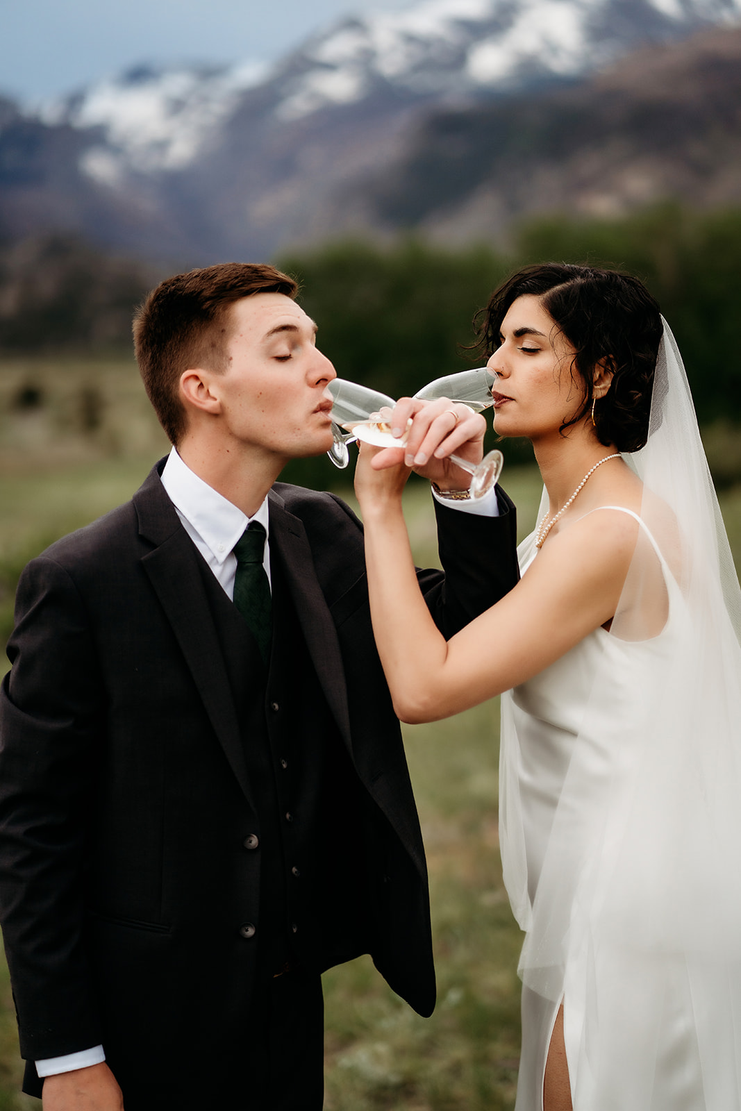 Couple links arms and sips champagne in front of the mountains, marking their elopement with a fun and romantic toast.