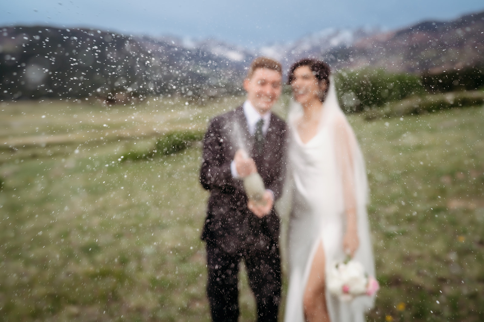 Blurred champagne spray captures the excitement as the newlyweds pop a bottle at their Colorado elopement location.
