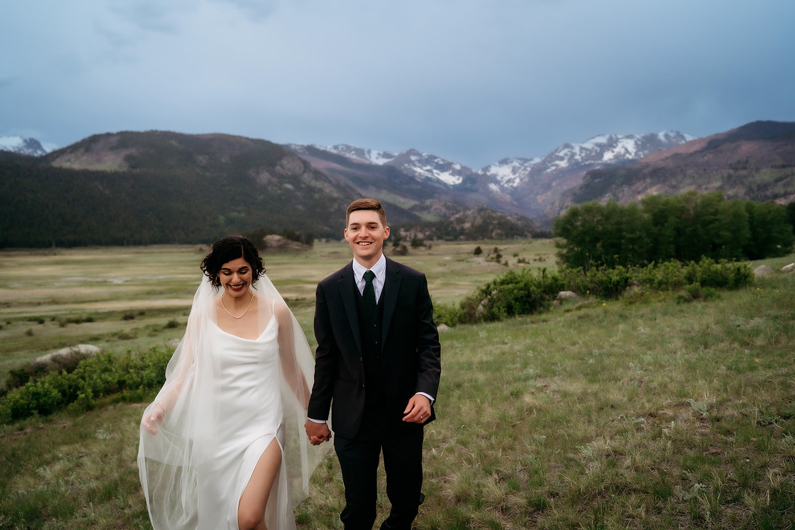 Just married couple laughing and holding hands in an open mountain valley, glowing after their elopement ceremony.