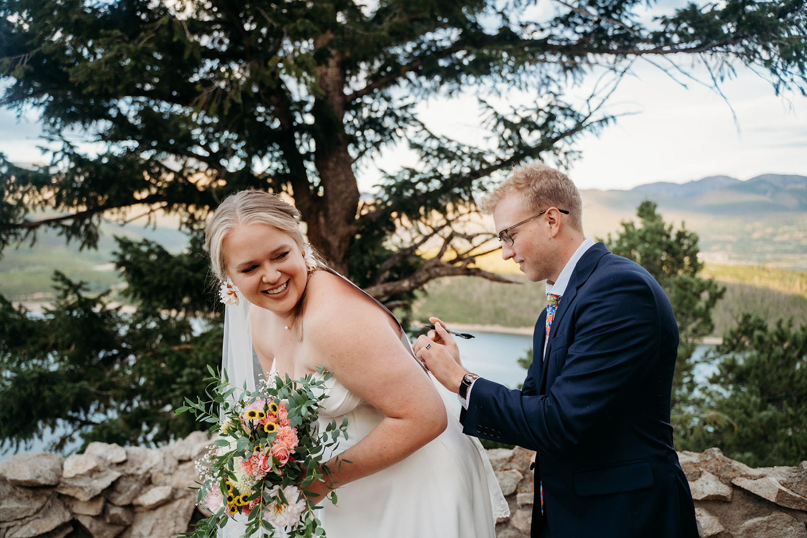 Groom playfully writing on bride’s back while she laughs, bouquet in hand, during candid wedding photos.