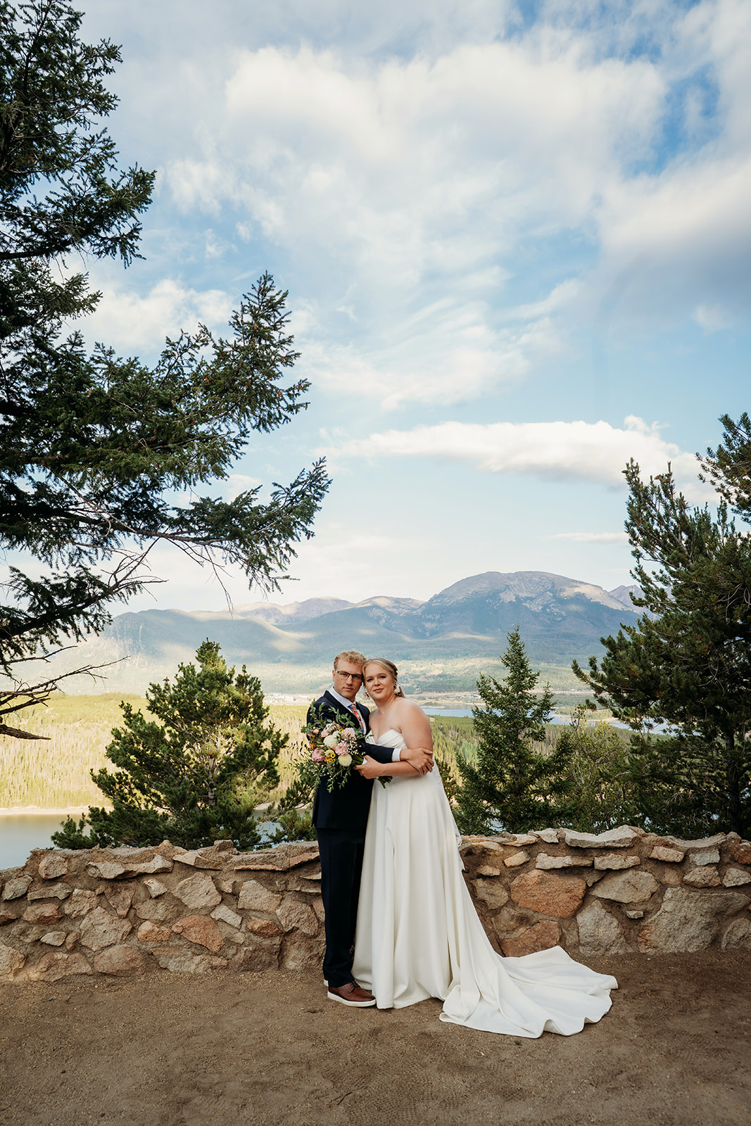 Couple standing arm in arm with mountain views, bouquet in hand, celebrating their outdoor ceremony, by Denver elopement photographer.