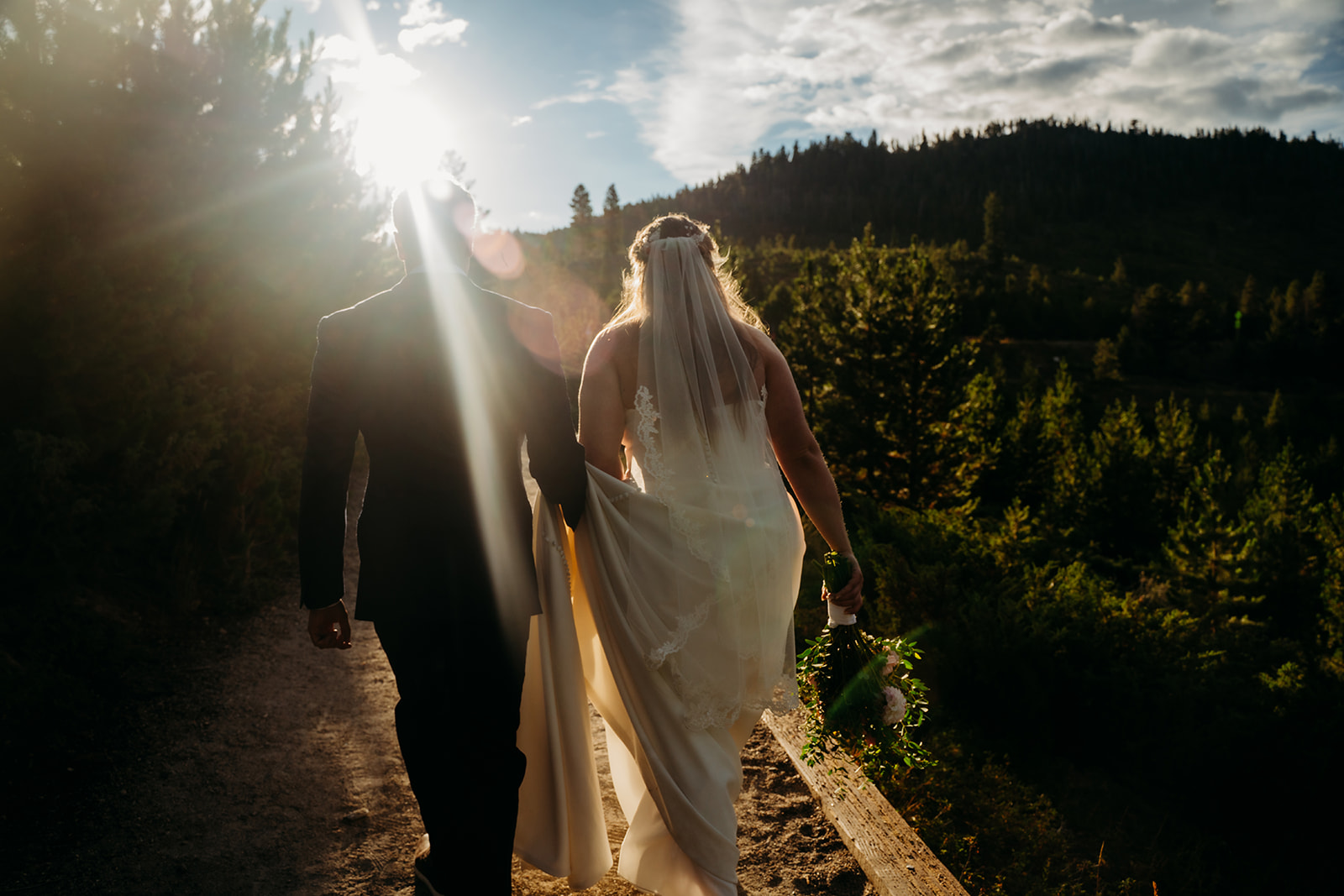 Couple sharing a romantic kiss on a mountain path with sweeping alpine views and dramatic sky.