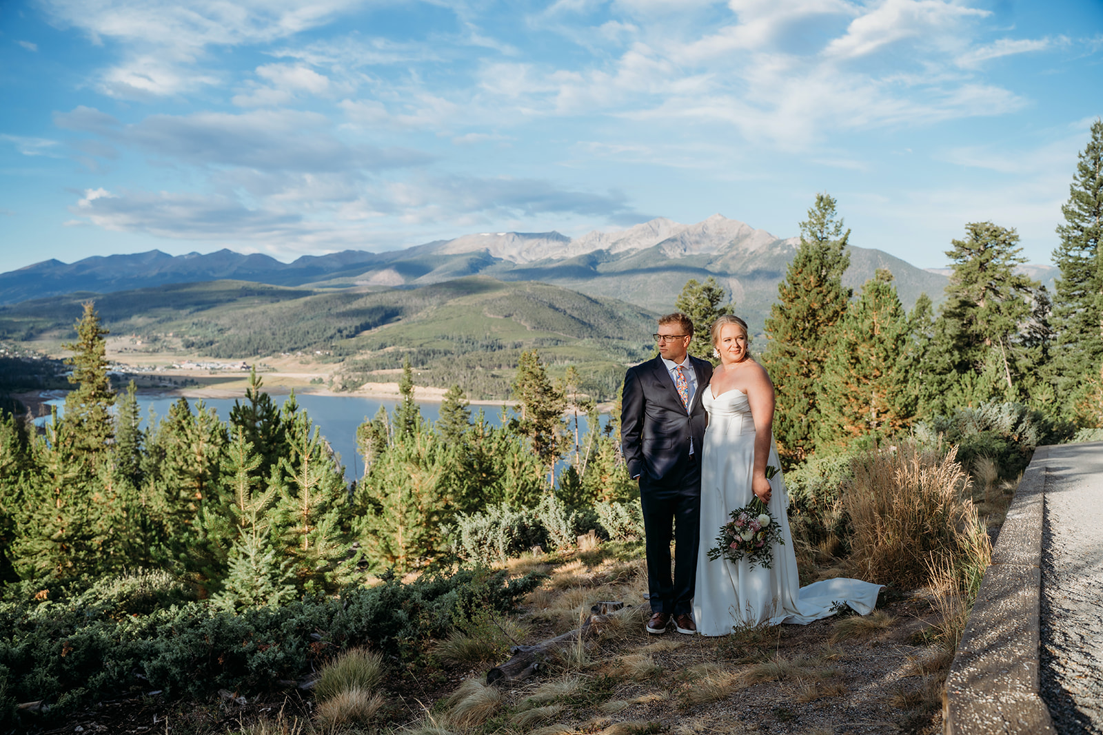 Couple posing with mountain and lake views behind them, standing close together in golden afternoon light.