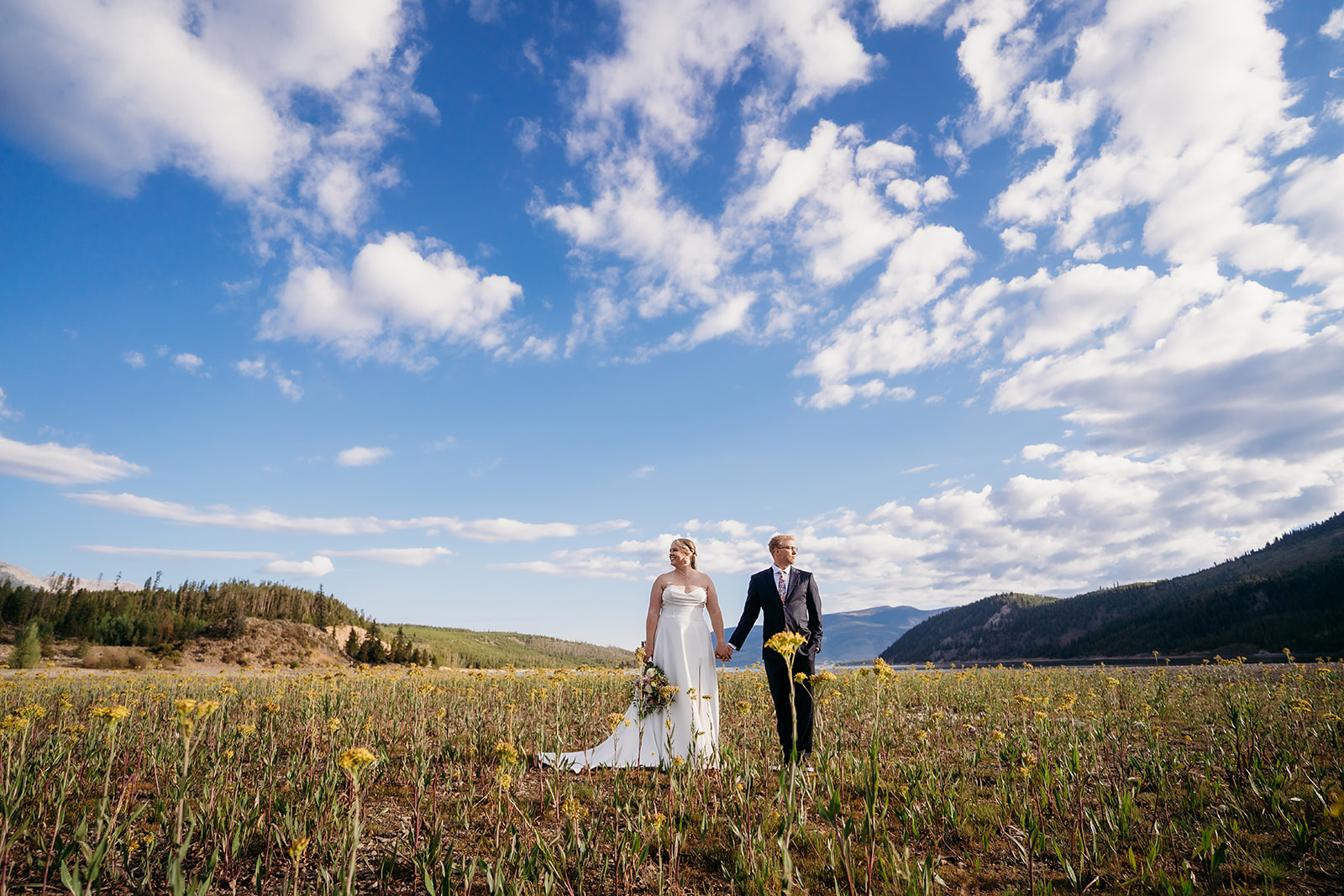 Bride and groom holding hands in a wildflower field under a bright blue sky, captured by a Denver elopement photographer.