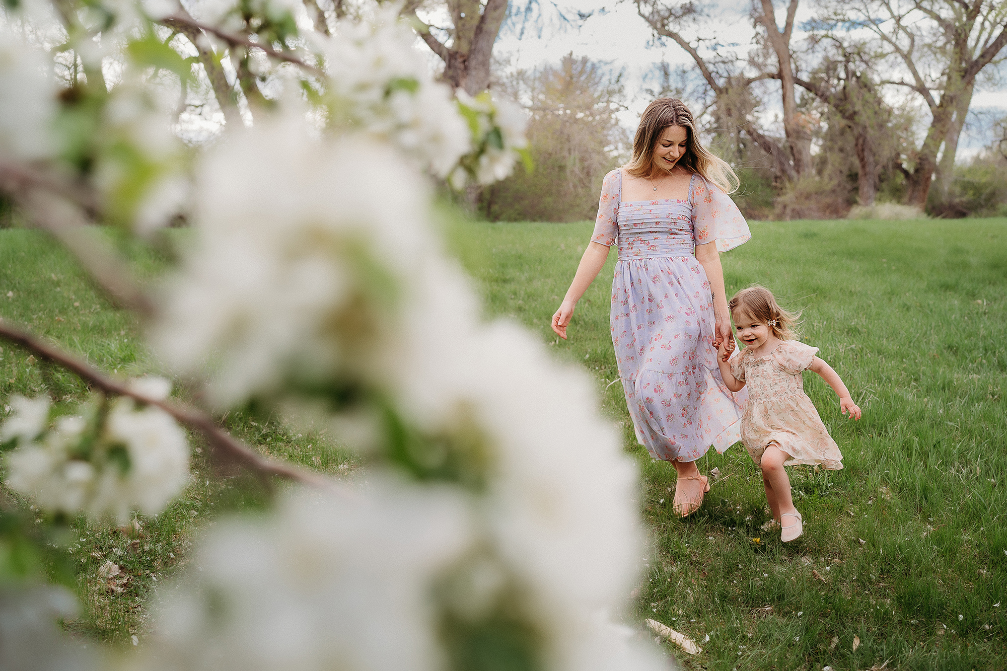 Mother and daughter running through a green field in pastel dresses, a playful example of family photo outfits.
