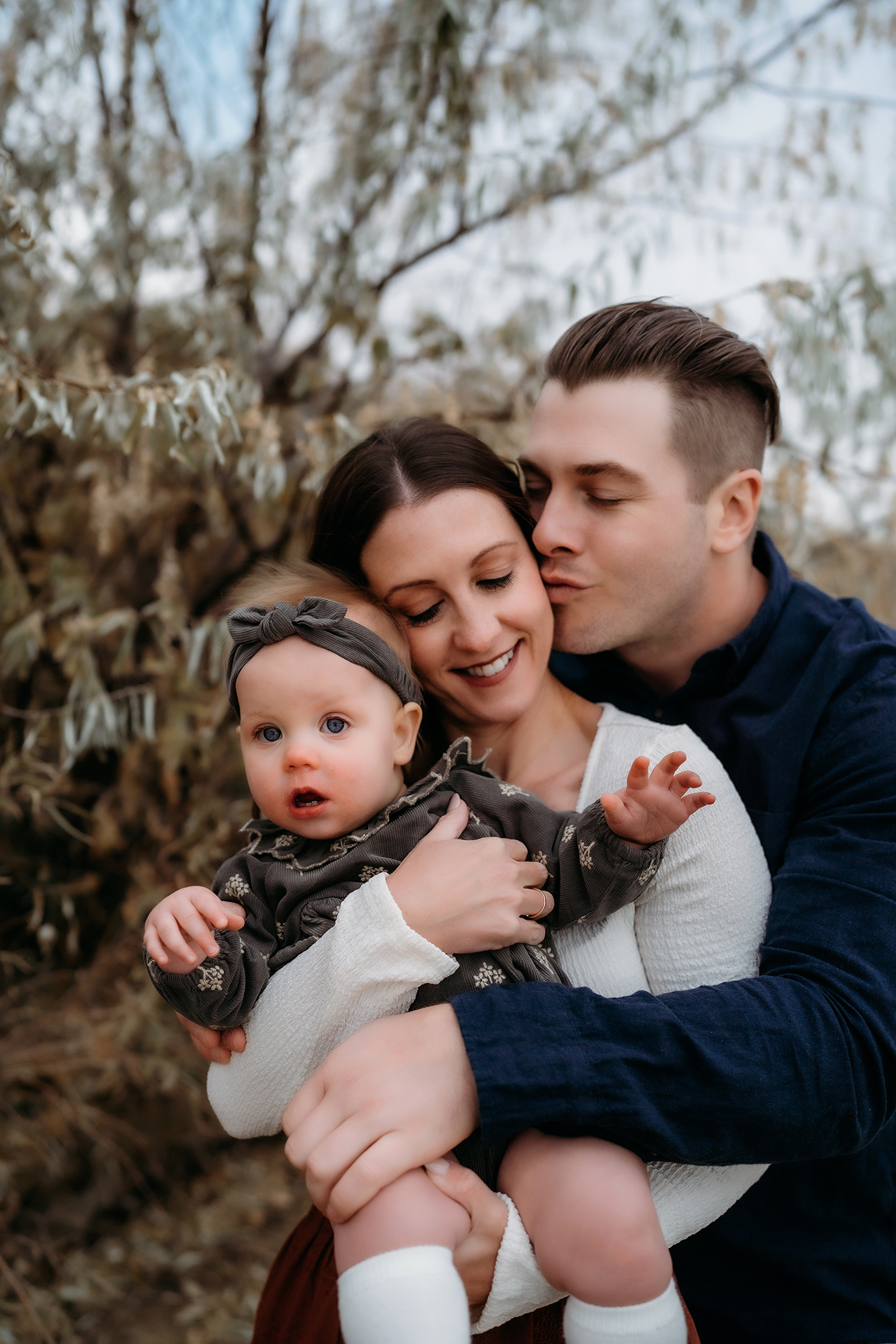 Close-up of parents holding their baby, dressed in soft fall tones for outdoor family portraits.