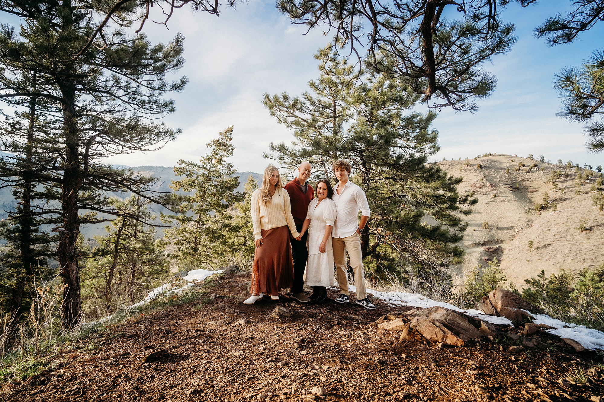 Family of four standing on a mountain overlook, wearing coordinated cream and earth-toned outfits for family photos.