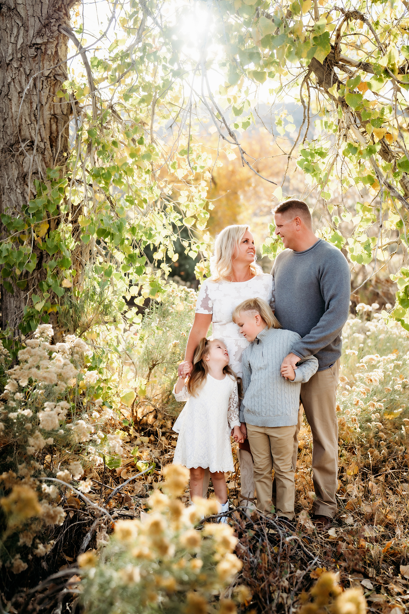 Family standing together under golden trees in autumn, wearing warm-toned outfits for family photos.