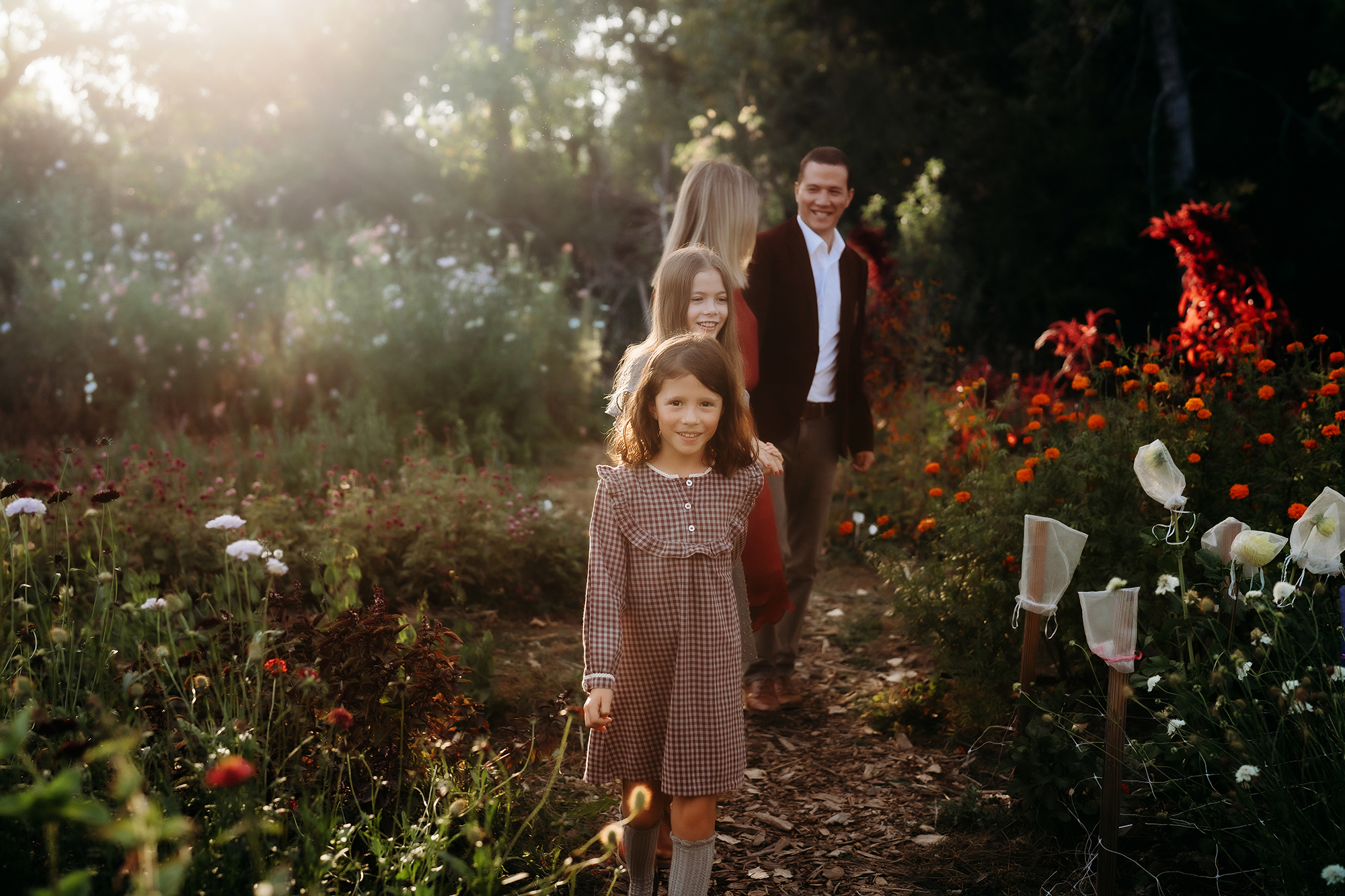 Young girl smiling while walking through a garden path with her family in the background.