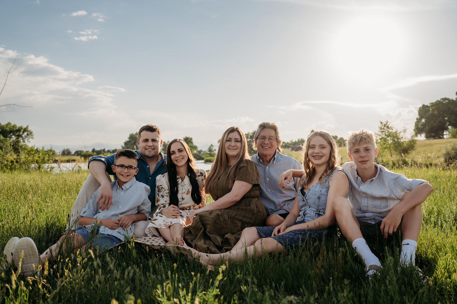 Extended family sitting together in a grassy field at sunset, coordinating their outfits for family photos.