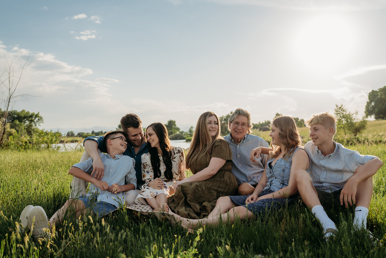 Large family sitting in the grass at golden hour, showing coordinated outfits for family photos in soft blues and earth tones.
