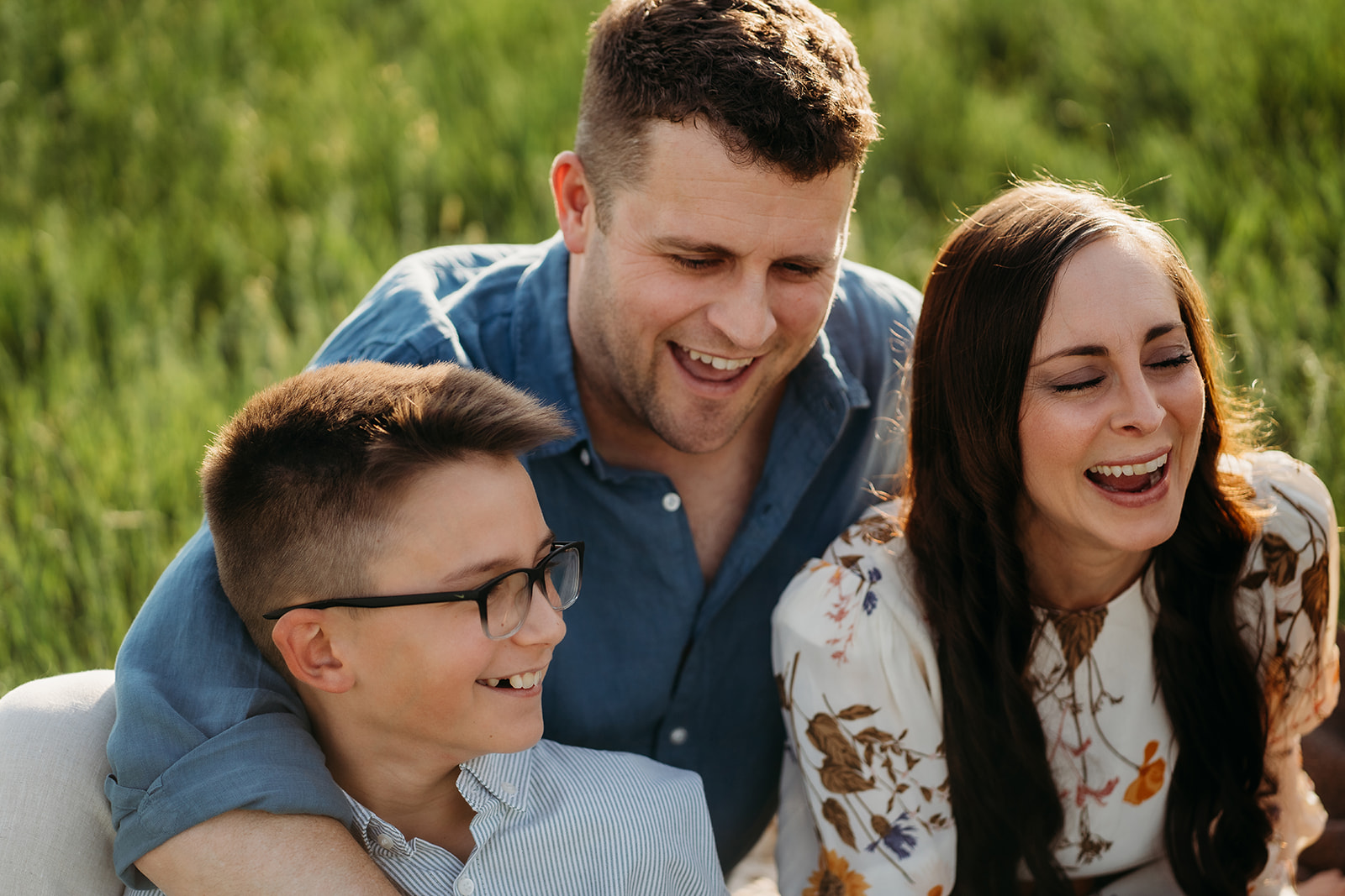 Close-up of parents laughing with their son in the sunshine, wearing playful summer outfits.