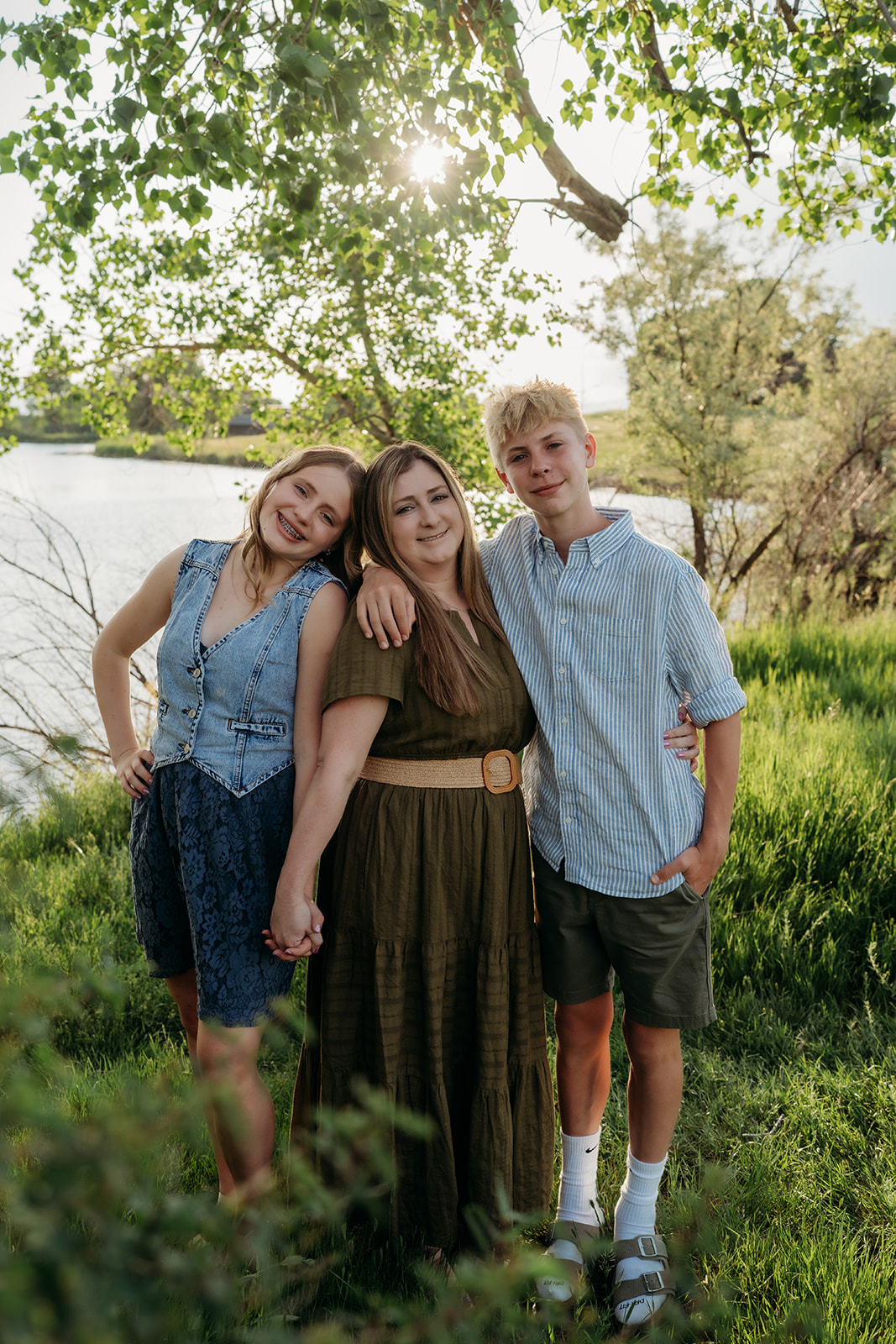 Mother with her two teens standing together under the trees, wearing earthy-toned outfits for family photos.