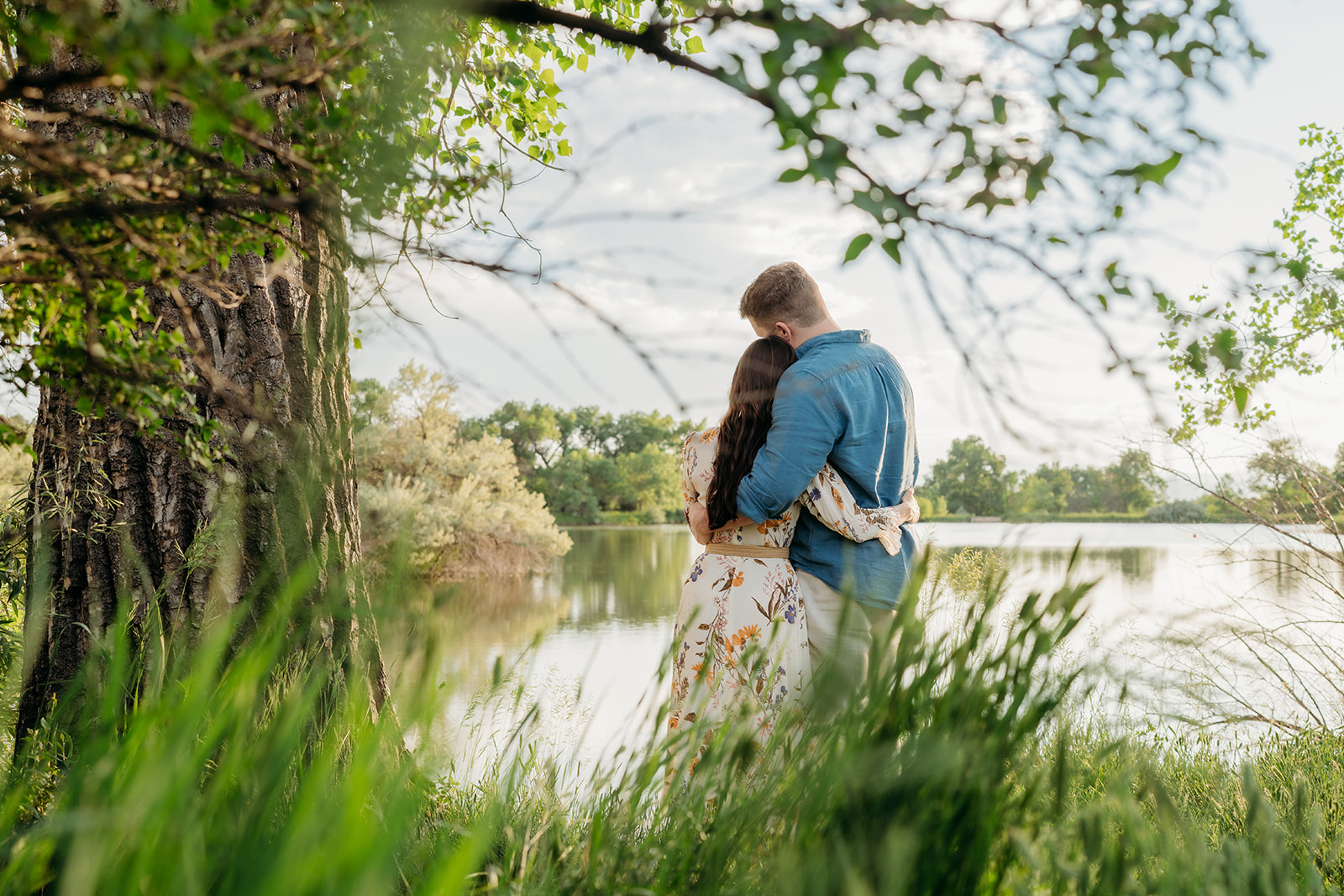 Couple embracing by a lakeside tree, showing romantic styling choices for family photos.