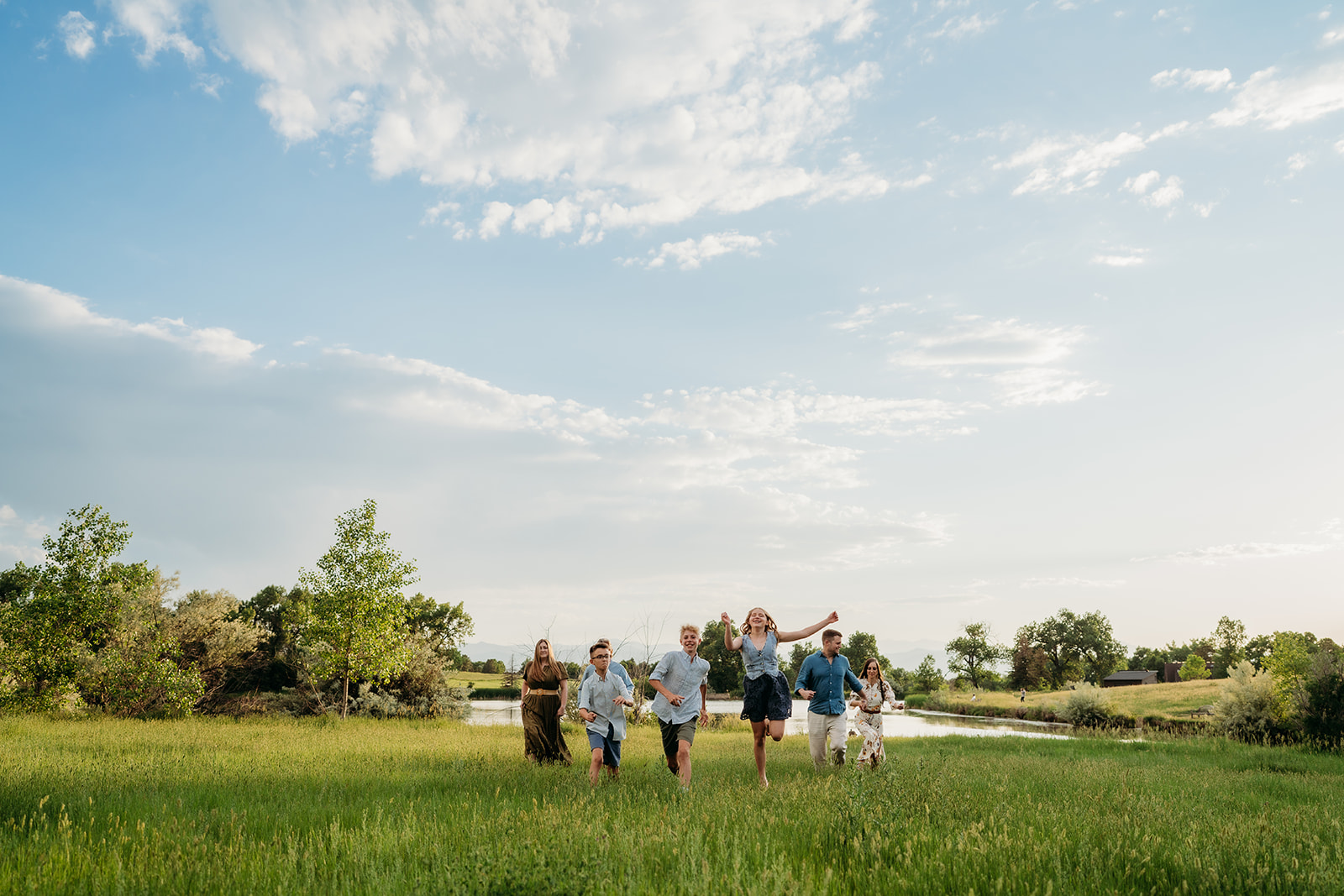 Large family running together across a sunny field in coordinated casual outfits for family photos.
