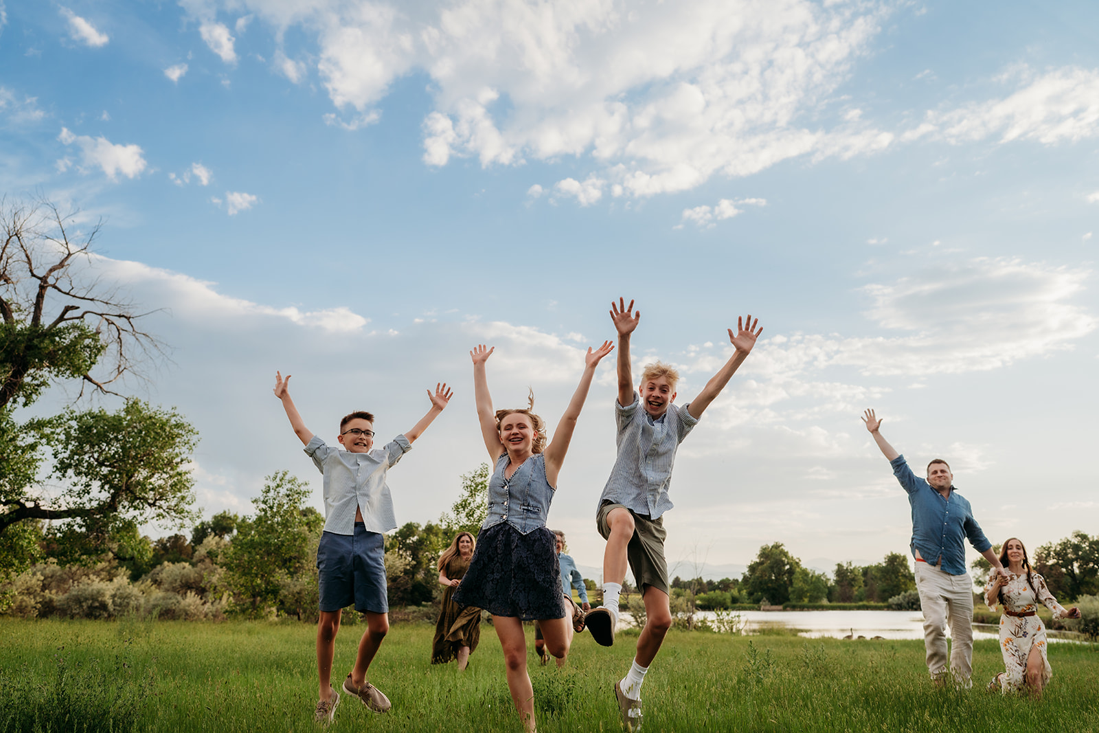 Family running and jumping in a green field, celebrating in casual coordinated outfits.