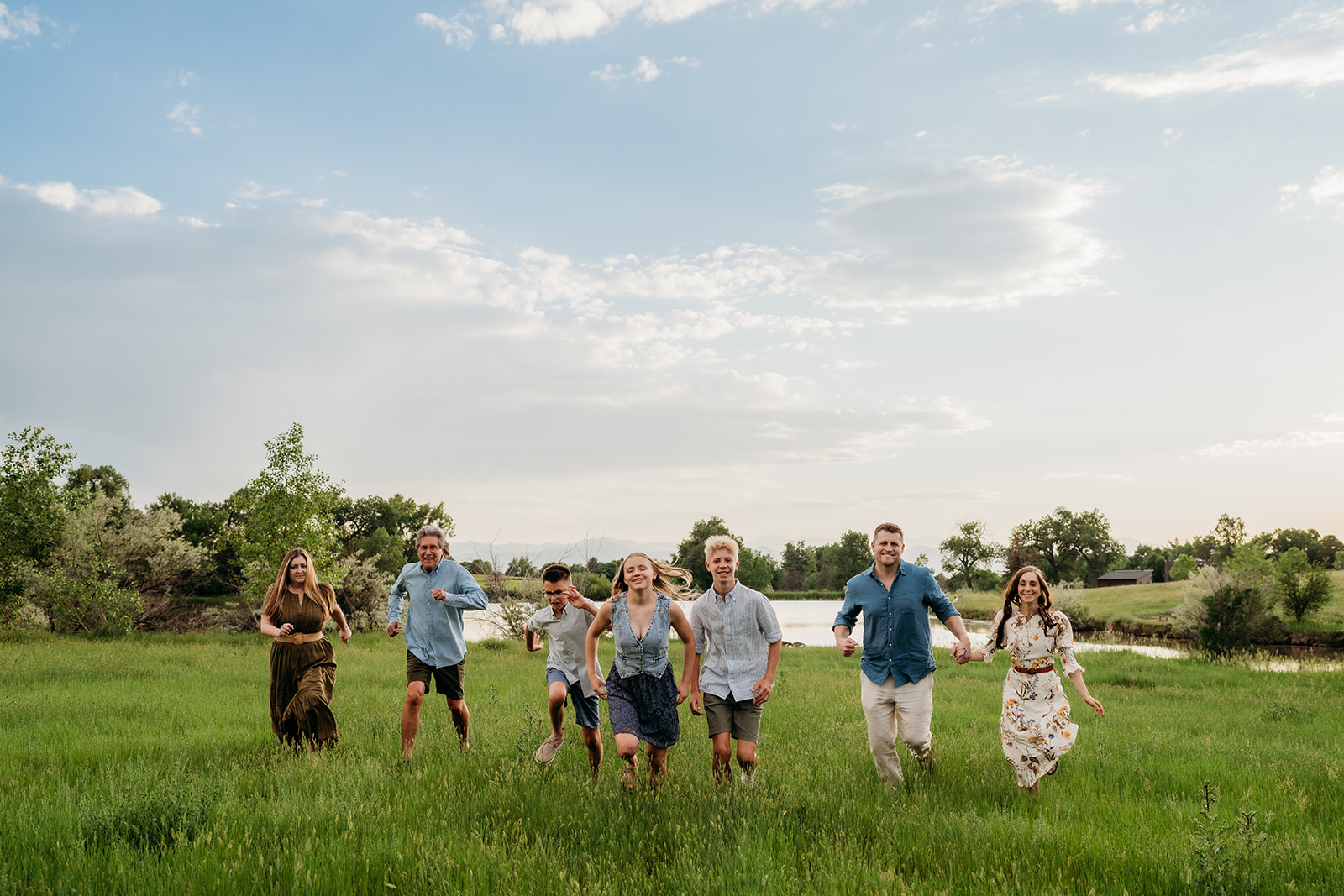 Large family running across a meadow near a lake, their outfits for family photos blending casual and coordinated styles.