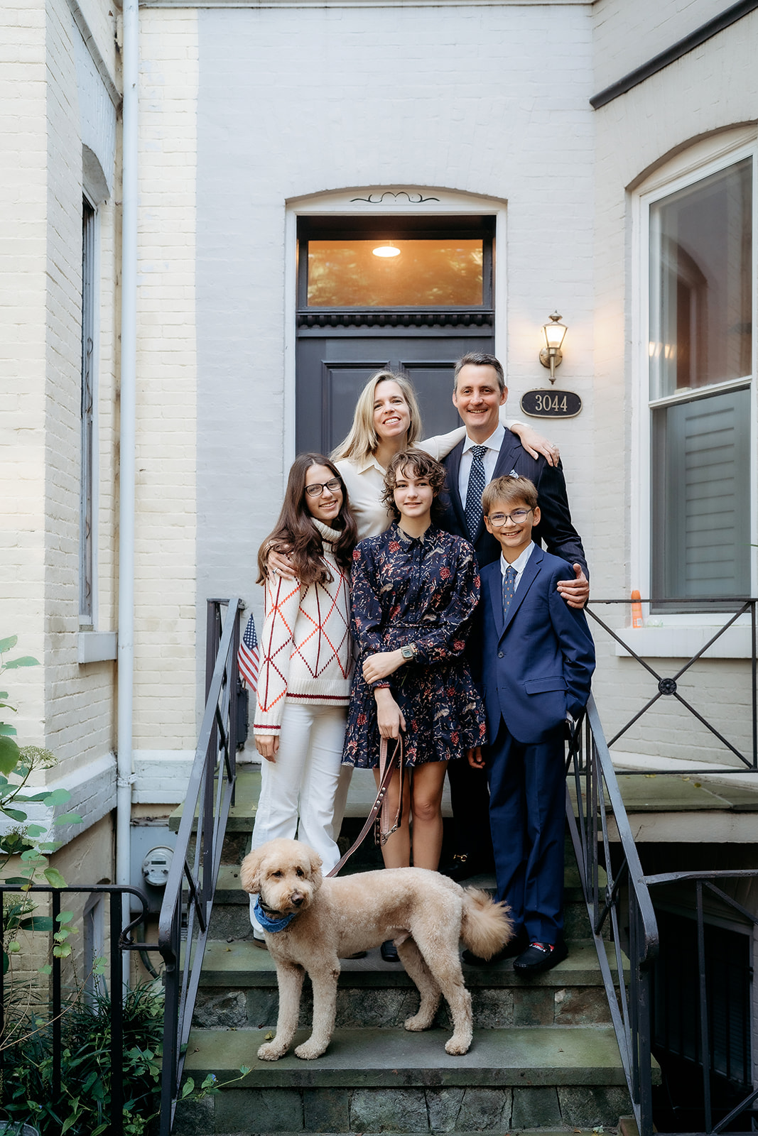 Family stands together on the front steps of their home, with their dog in front—capturing a cozy and personal annual family photo.