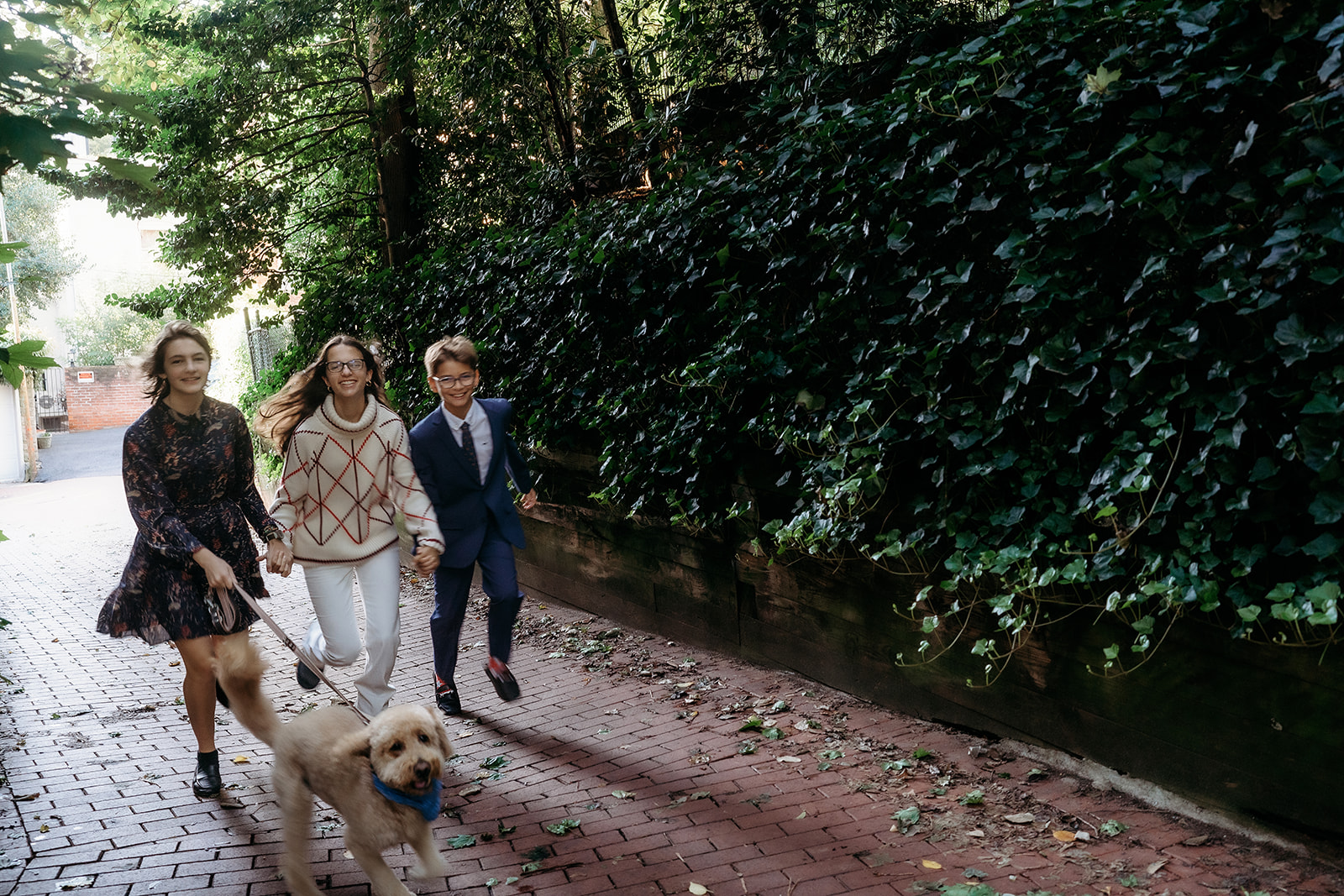 Sisters and brother jog with their dog along a shaded path, showing off their fun, candid side during a family session.