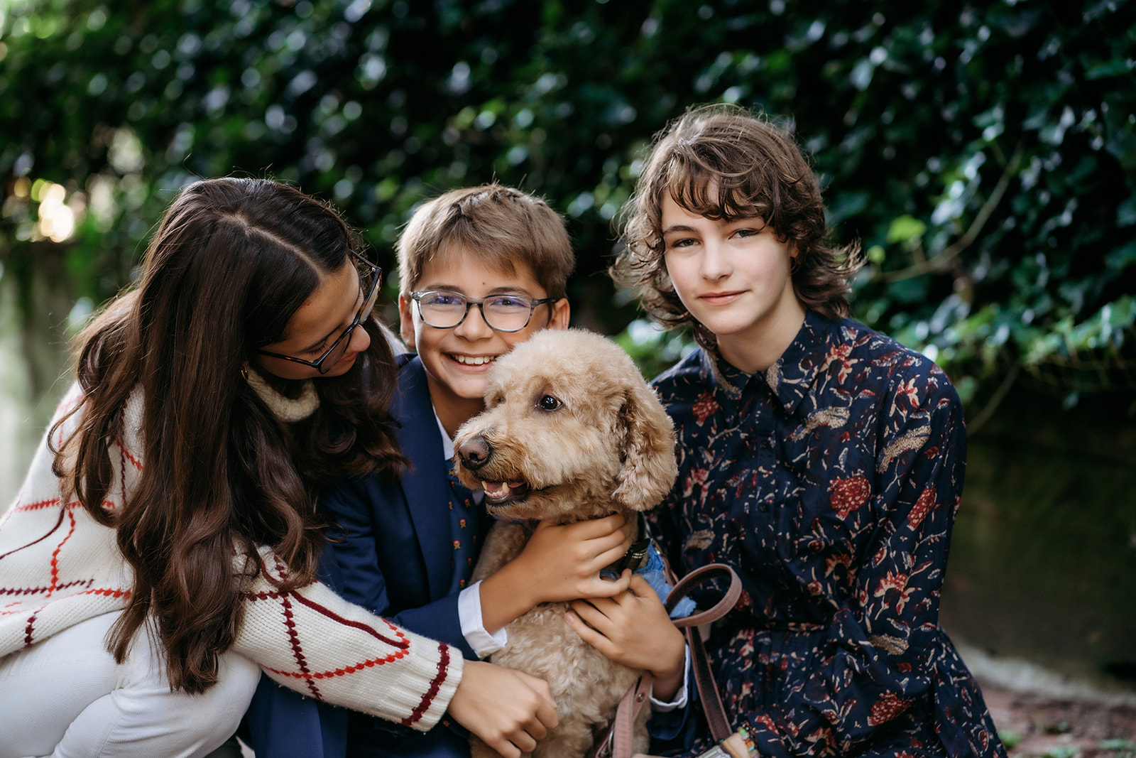 Three siblings cuddle their goldendoodle in a sweet close-up, full of laughter and love during their annual family photo session.