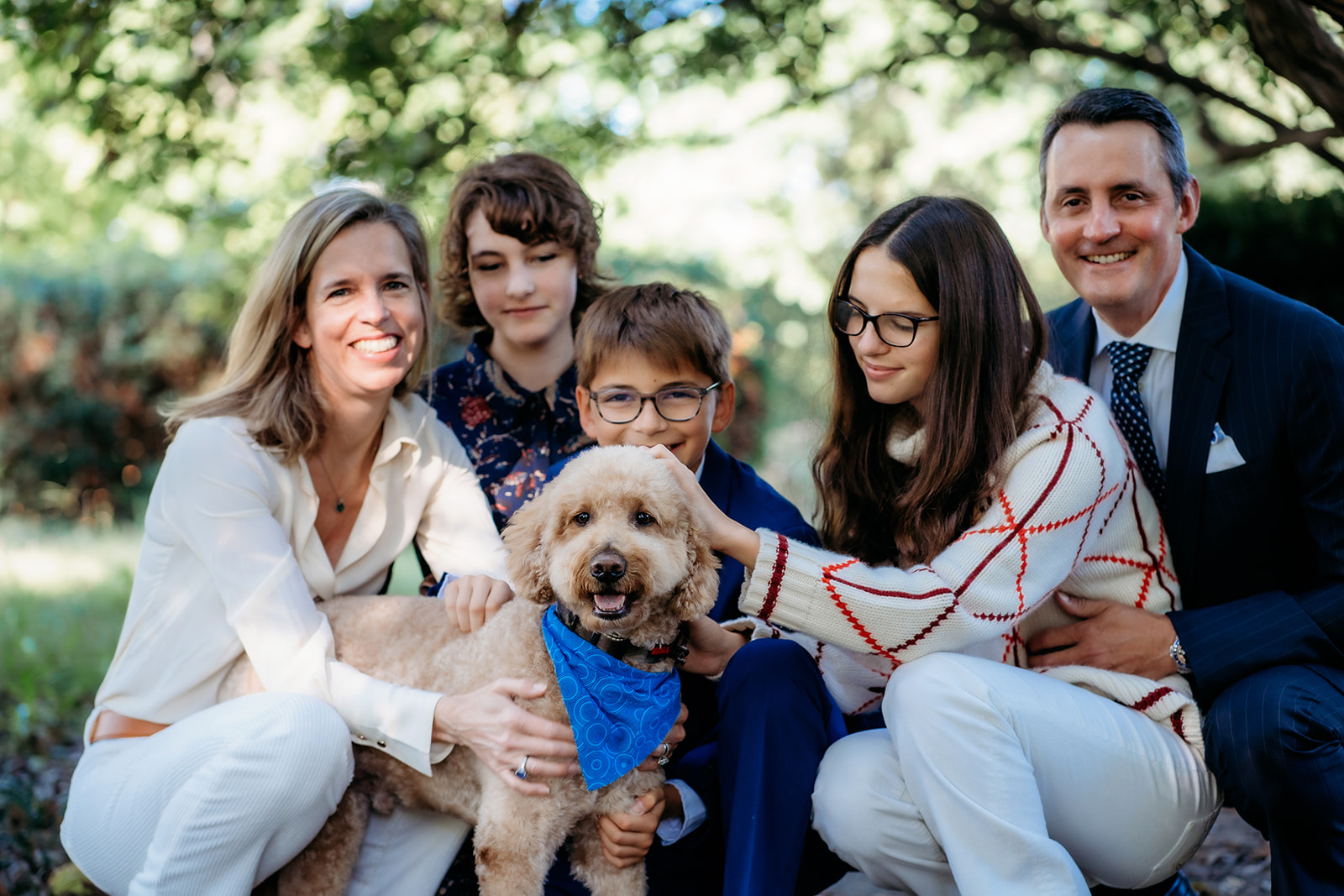 Family crouches together with their dog, sharing big smiles and sweet pets during their annual family photos.