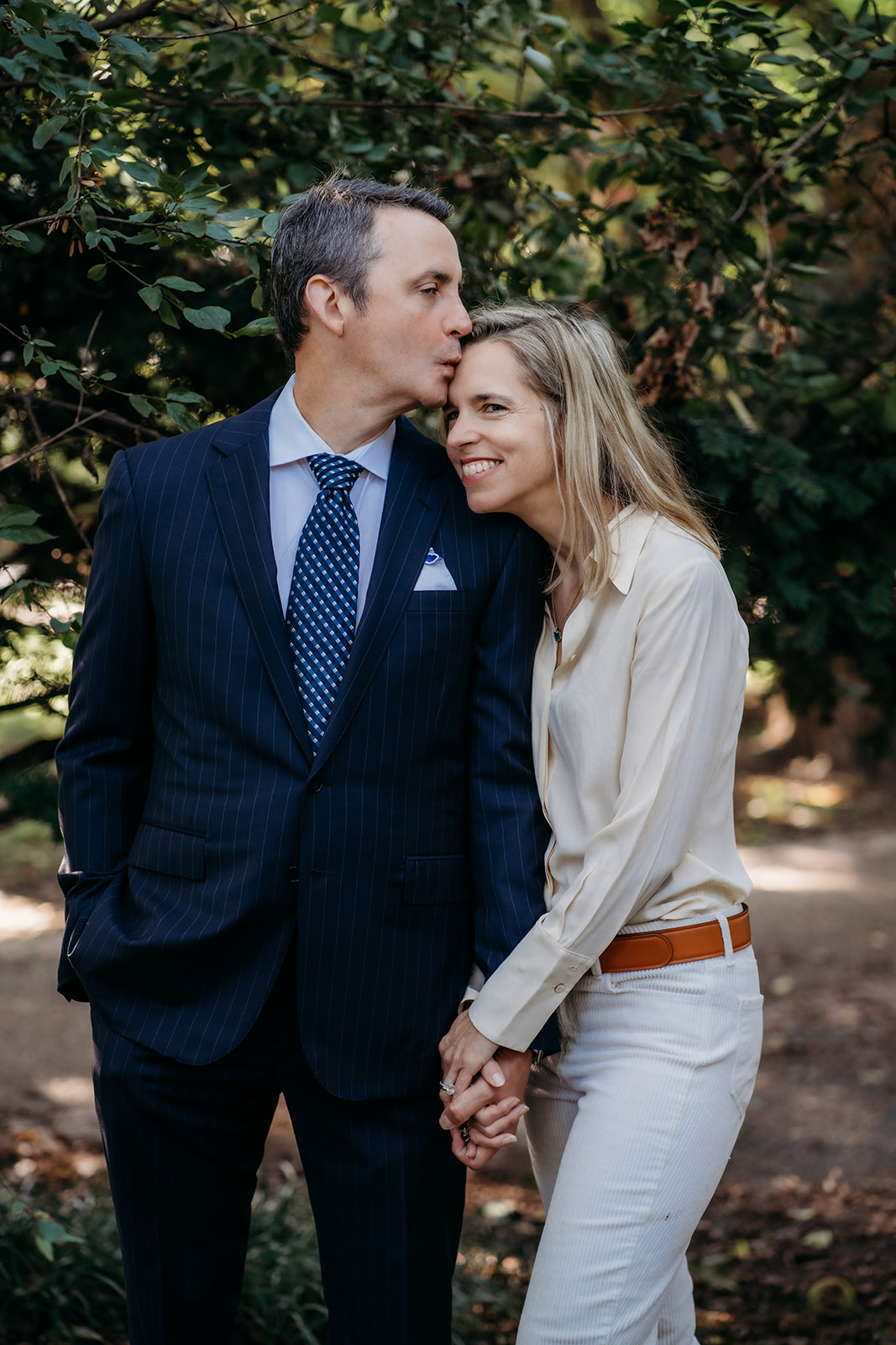 Husband and wife hold hands while husband kisses wife's forehead during annual family photos