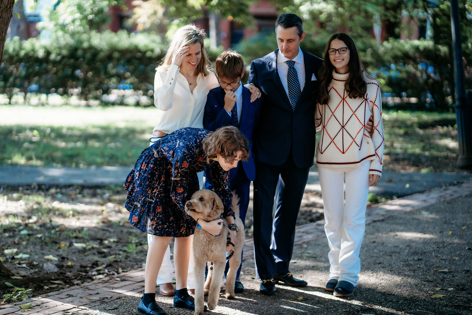 Family stands together smiling while daughter adjusts dog's leash during outdoor family photos in Colorado
