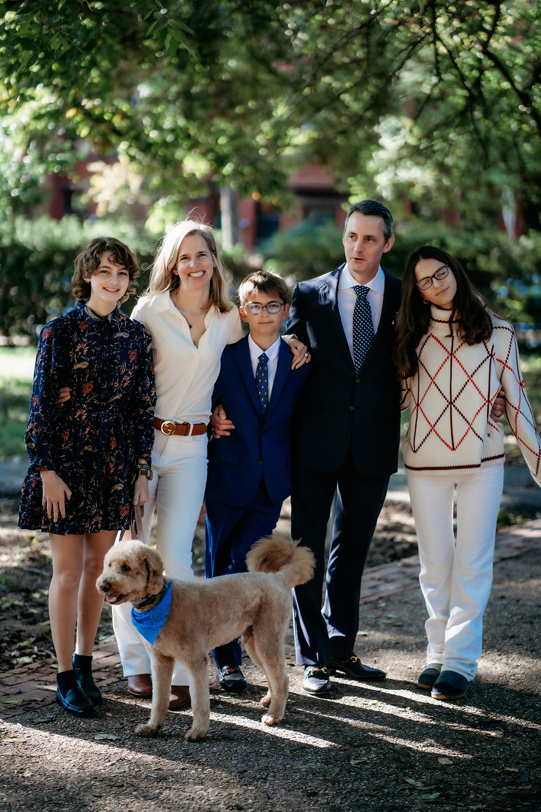 Family stands together smiling in park they visit every year with photos spending time together