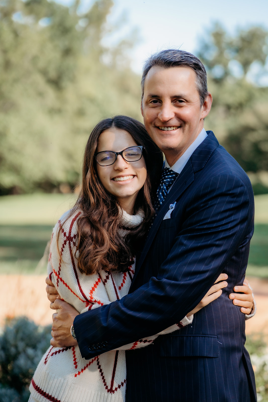 Dad and daughter smile wide and share a tight hug, capturing a joyful candid during their annual family photos.